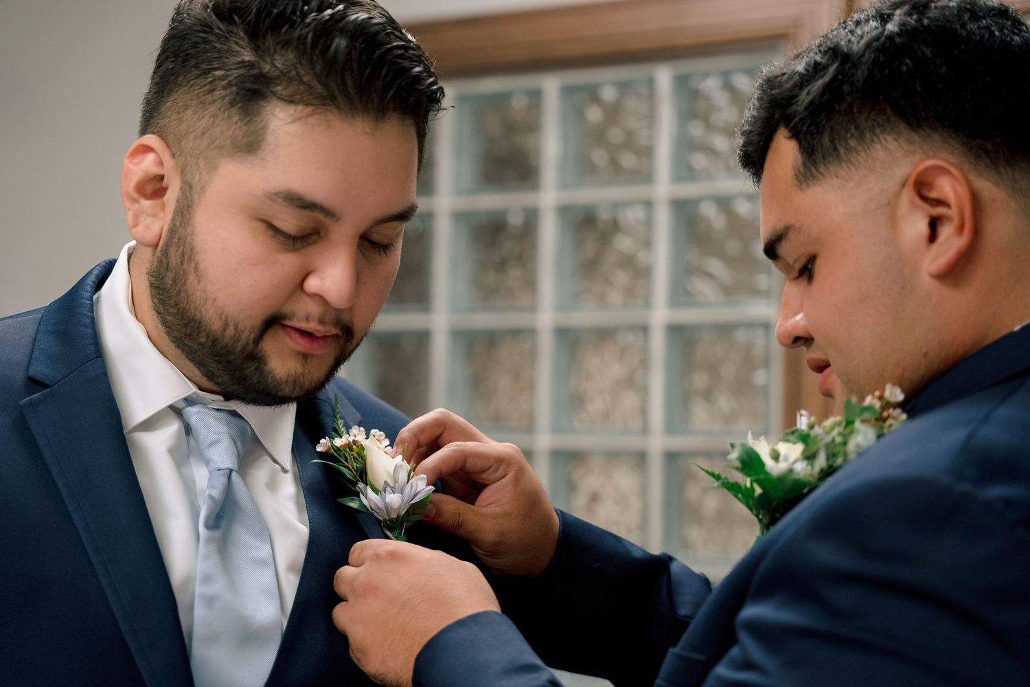 Two grooms share a tender moment during their wedding ceremony as they smell white floral boutonnieres.