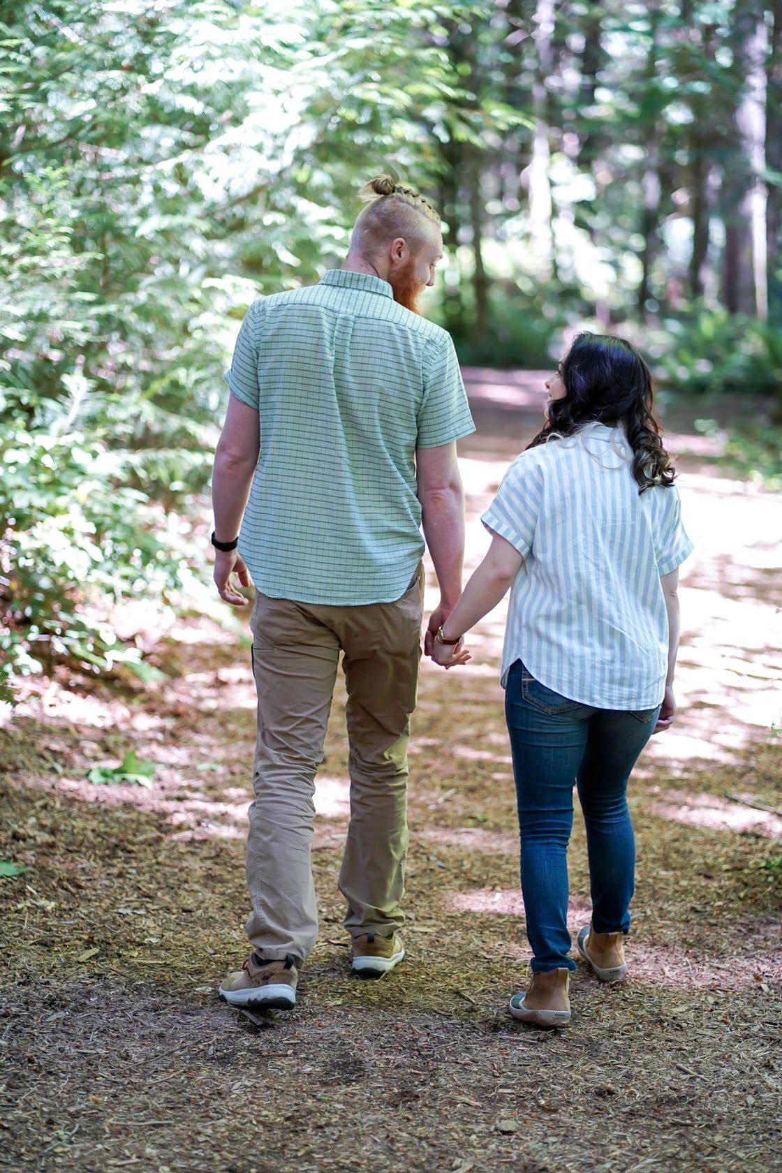 A couple walks hand in hand through a wooded forest path on a sunny day.