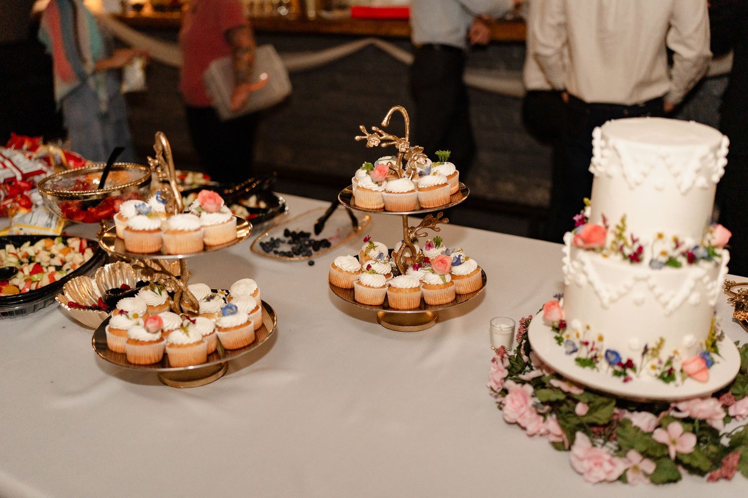 Wedding dessert table featuring tiered cupcake displays and a traditional white cake with floral decorations.