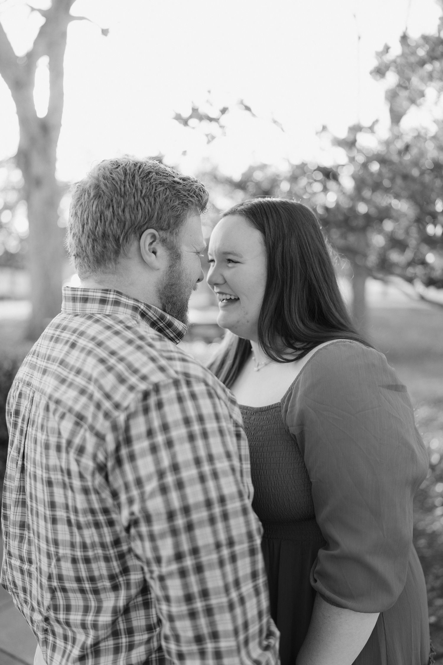 Black and white photo of laughing couple facing each other in an intimate outdoor engagement session.