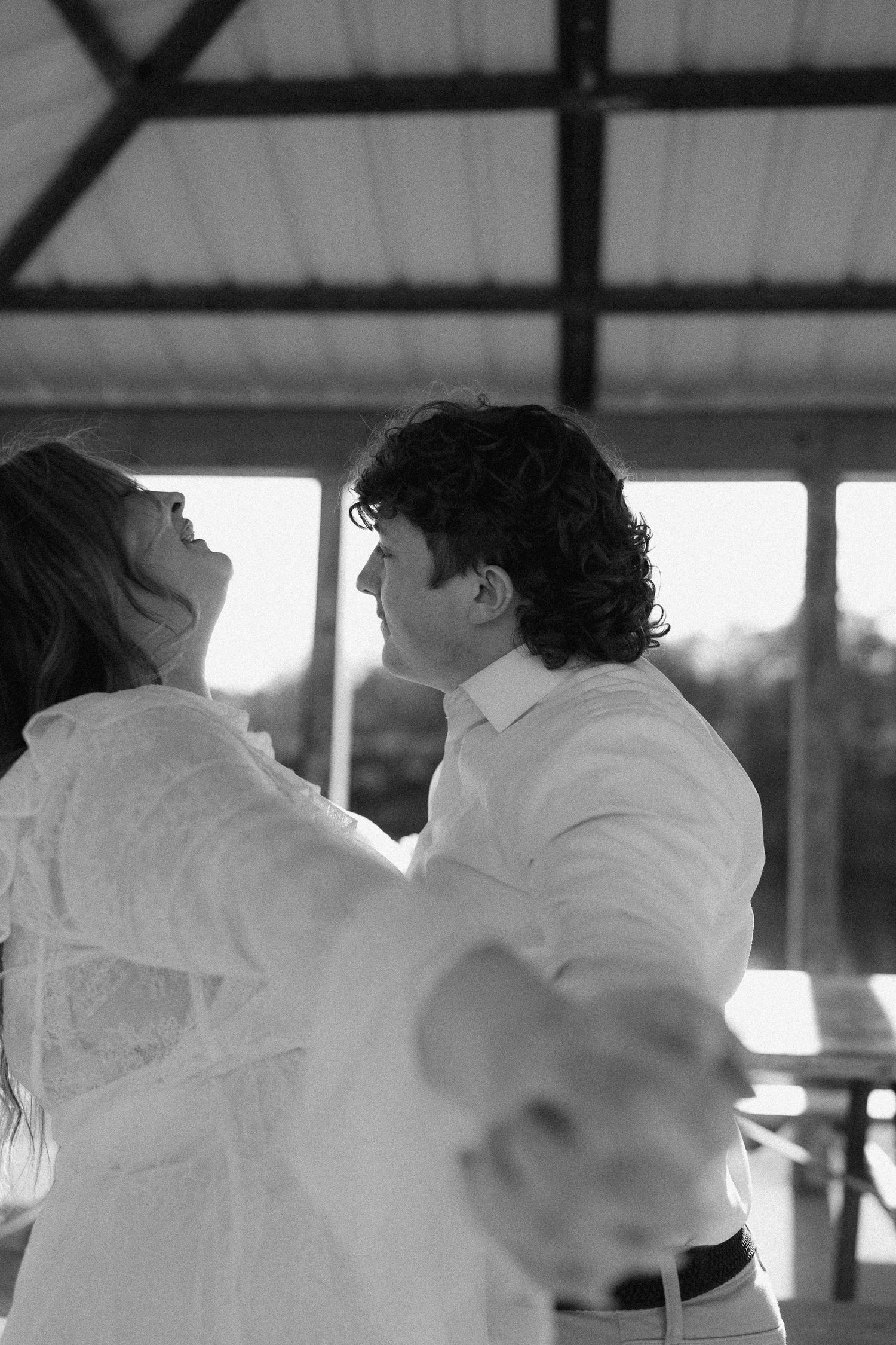 Black and white photo of couple dancing together joyfully under covered pavilion after engagement proposal.