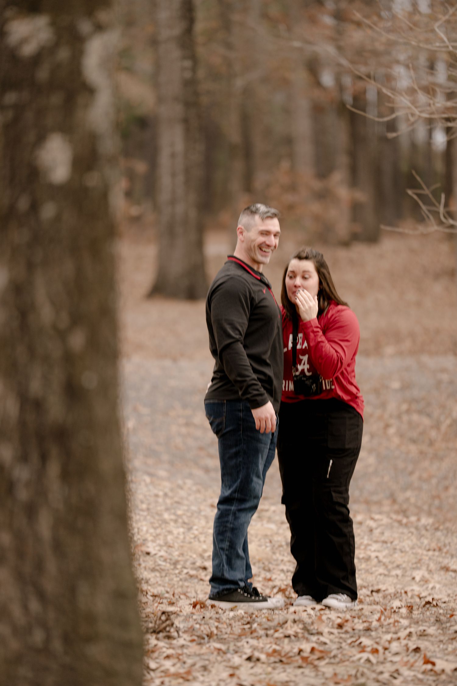 A romantic proposal moment captured in a wooded area with fallen leaves during autumn.