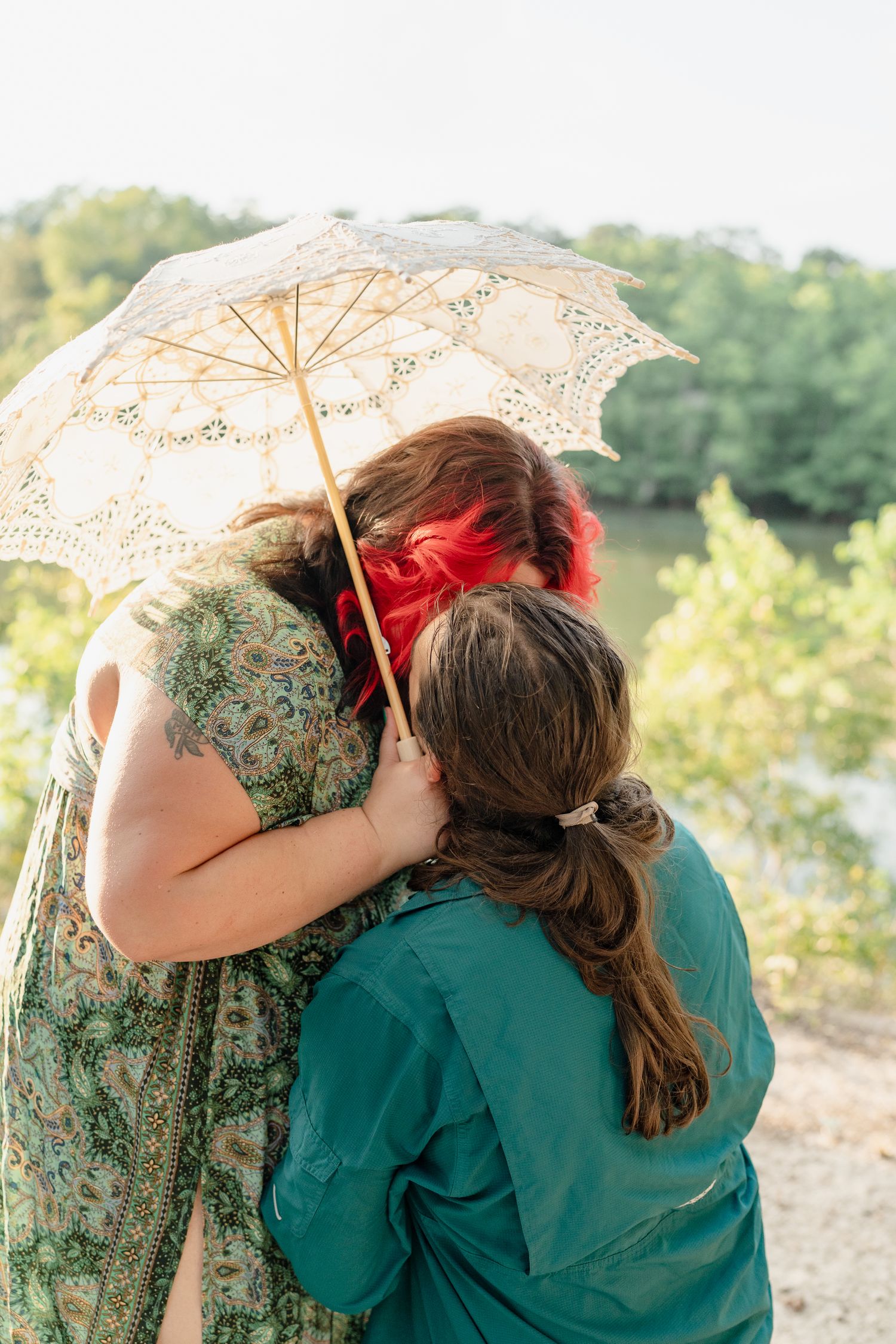 A couple shares an intimate moment under a delicate lace parasol in a natural outdoor setting during golden hour.