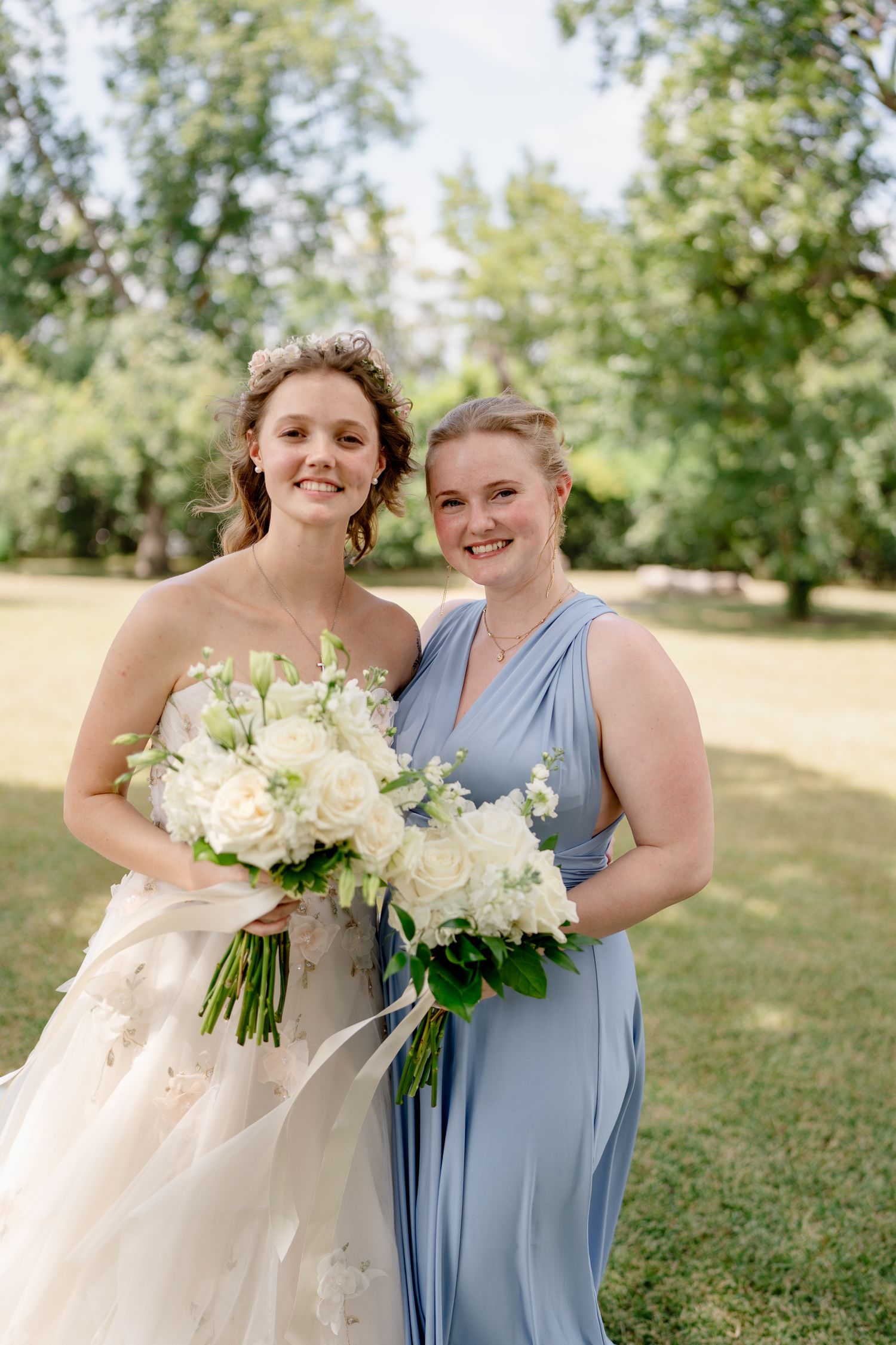 Bridesmaids in powder blue dresses hold elegant white rose bouquets during outdoor wedding photos.