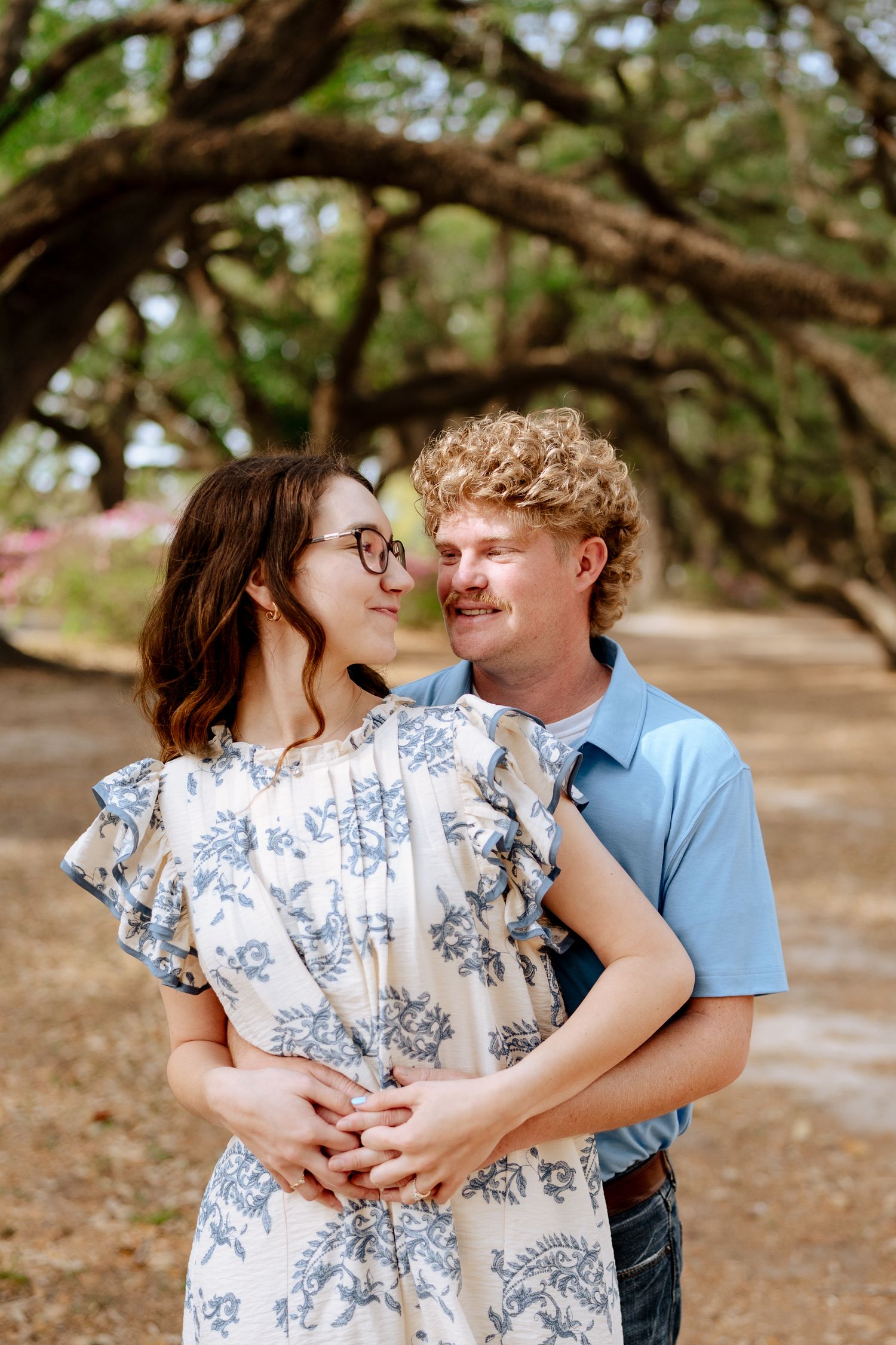 Tender embrace between couple in casual wear under sprawling oak branches.