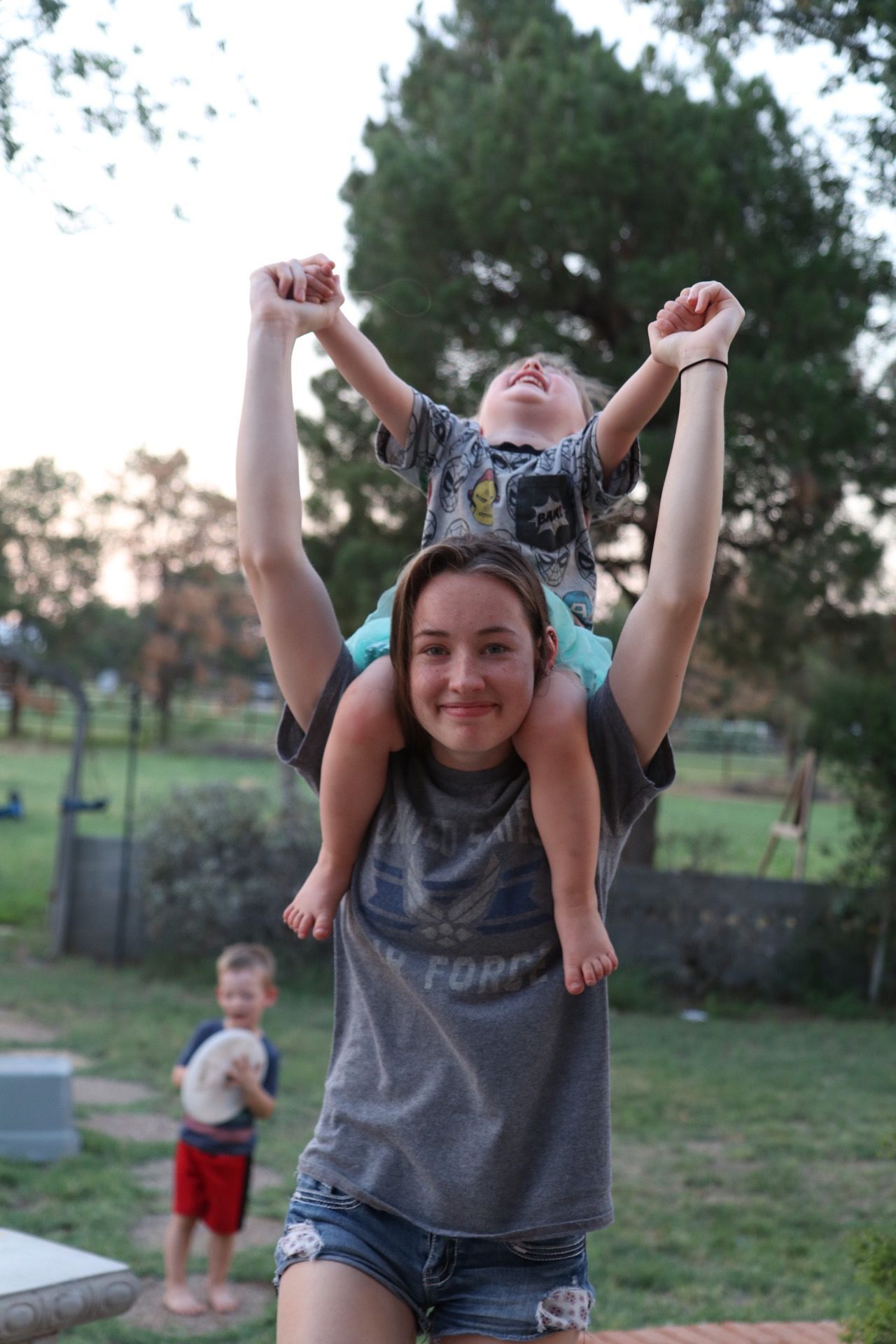 A playful piggyback ride in a park with trees and grass in the background.