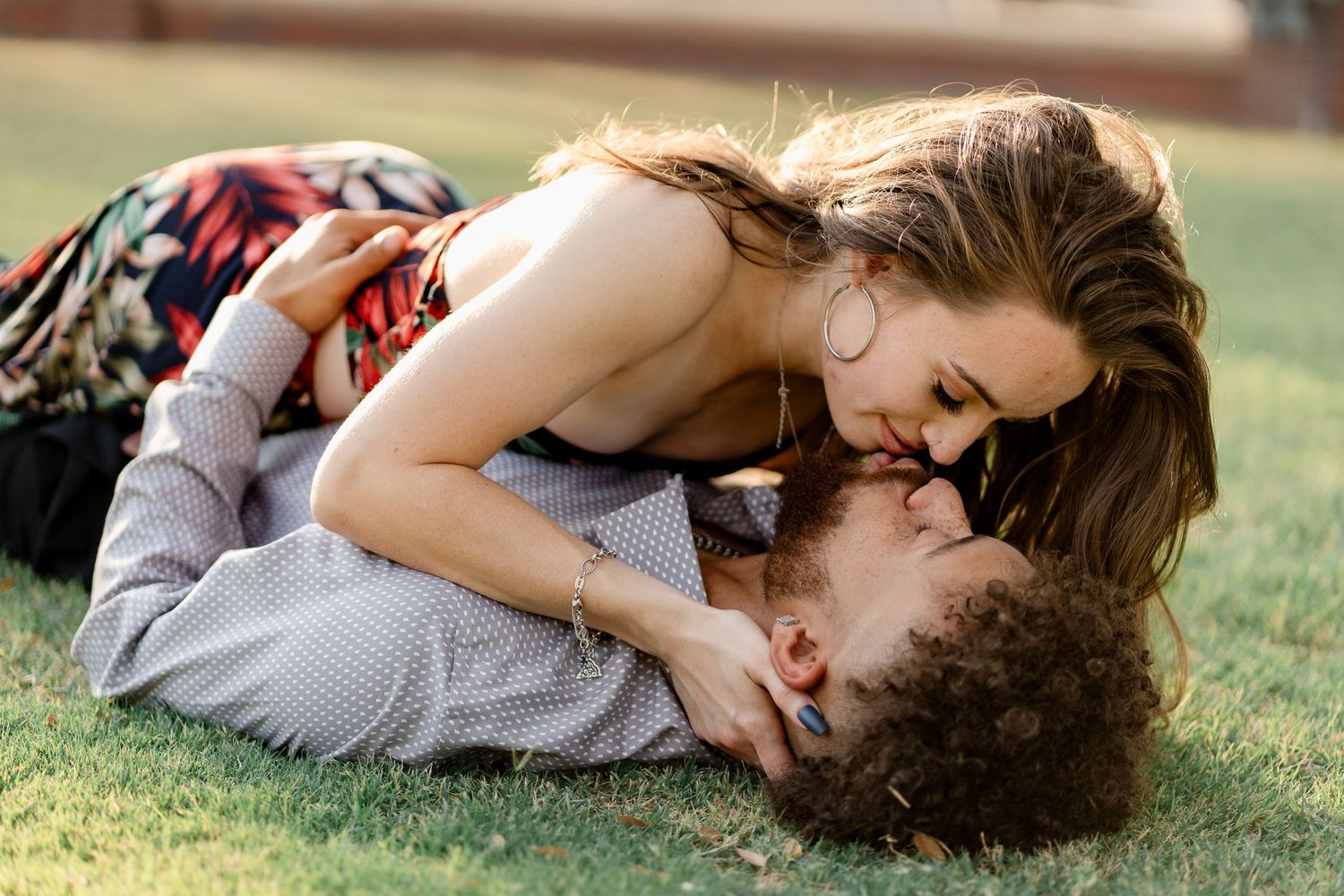 A couple shares intimate moments while lying on grass during sunset.