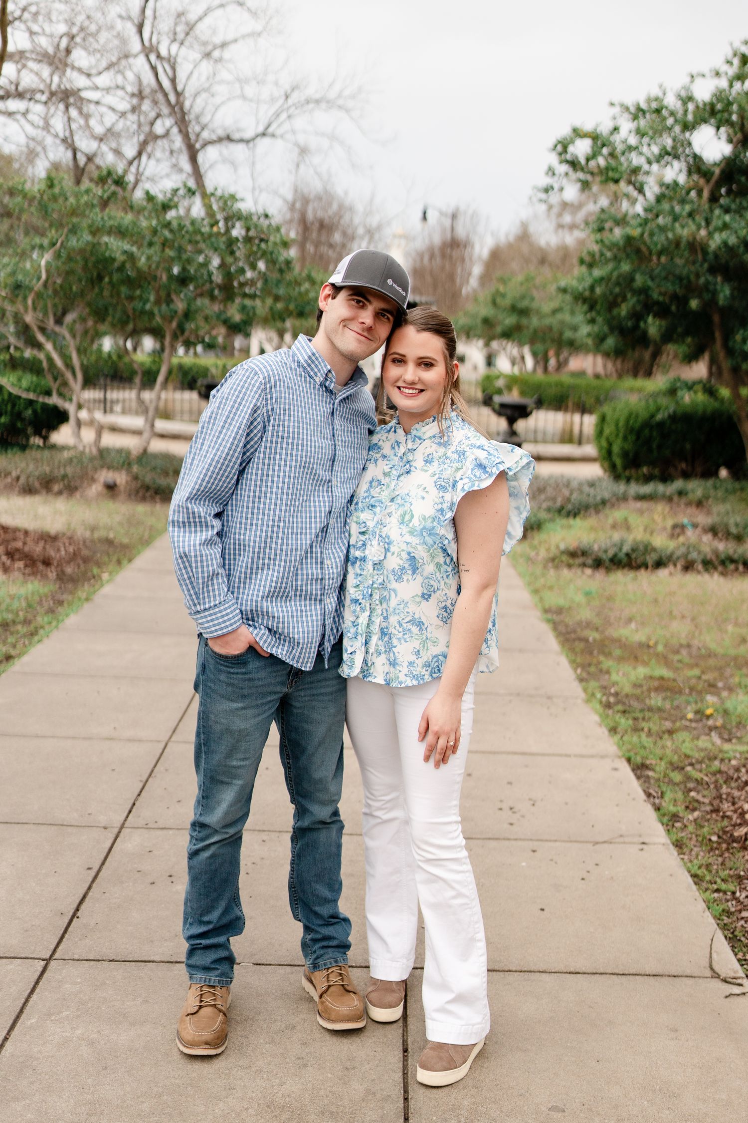 A couple poses casually on a garden path wearing coordinating blue and white outfits.