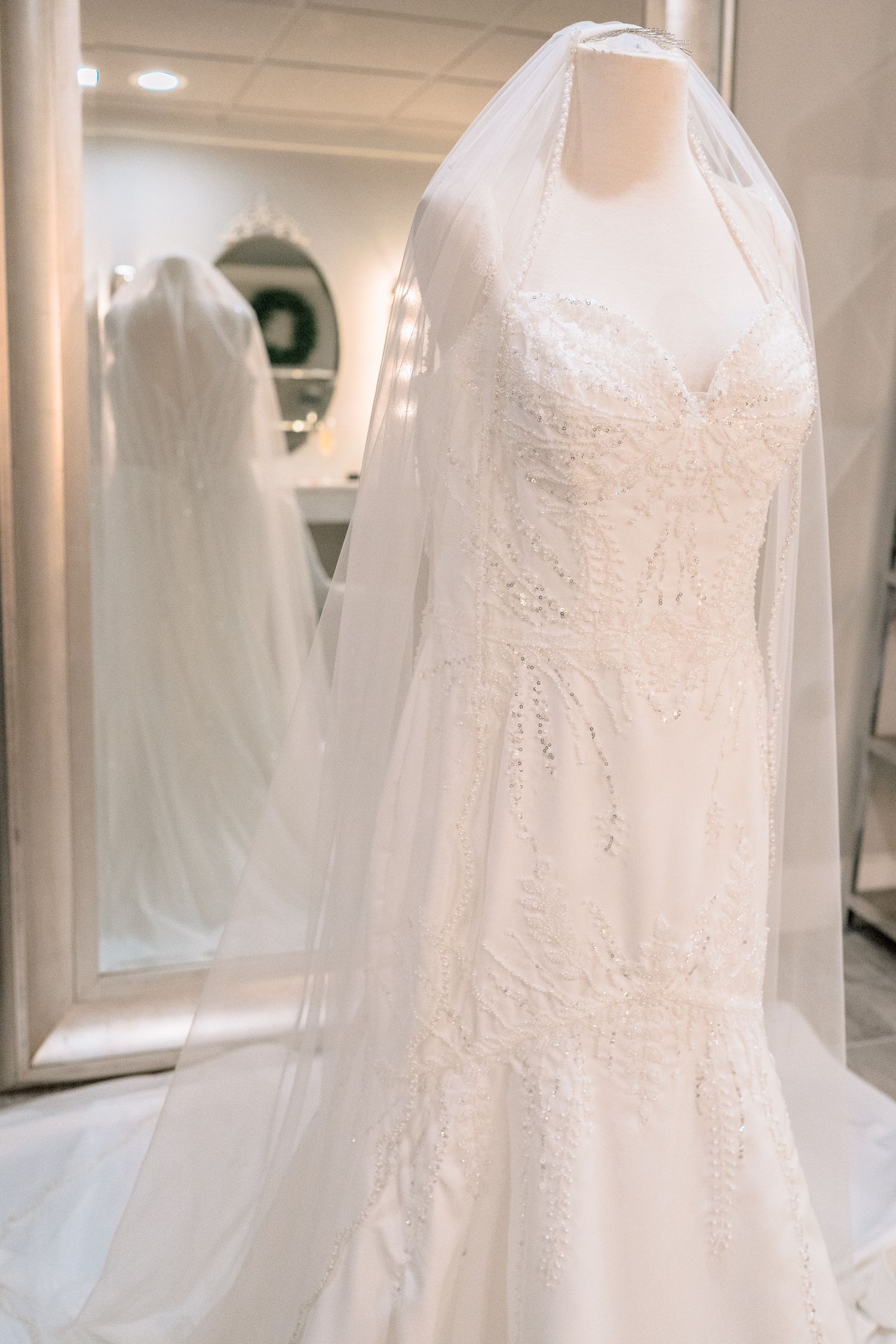 Elegant white lace mermaid wedding dress with veil on mannequin in bridal boutique.