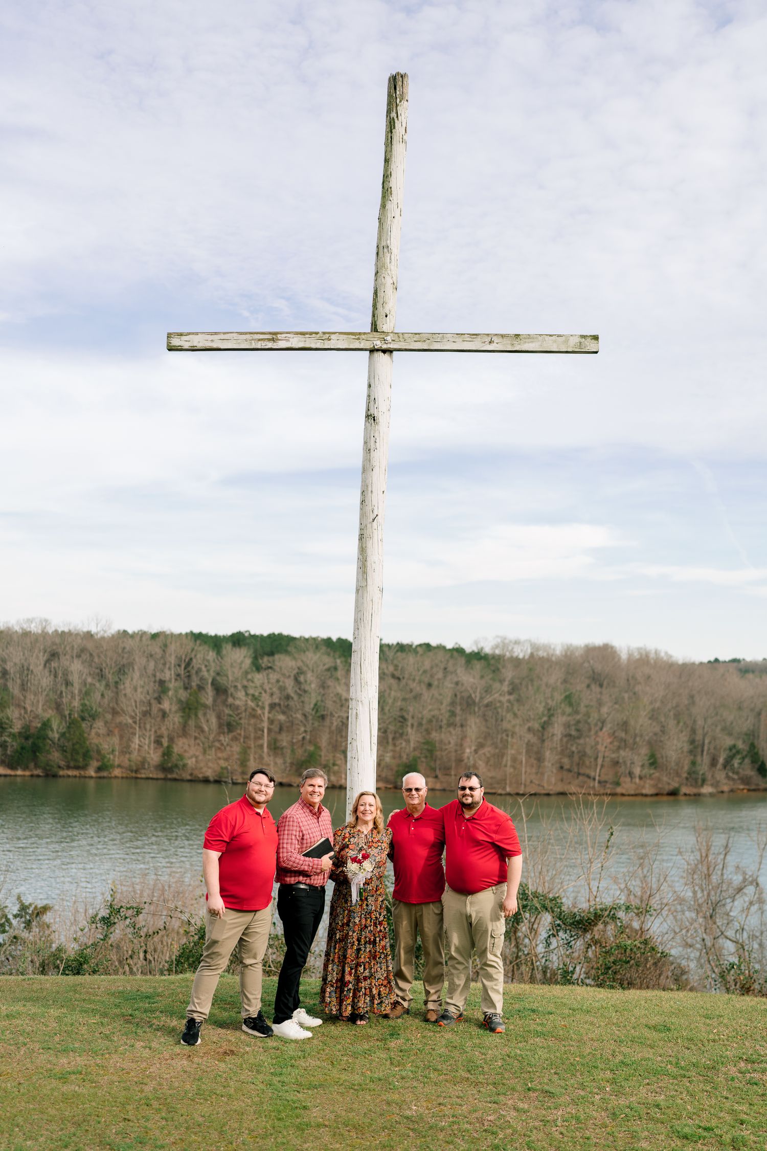 Family of five posing in front of a large wooden cross overlooking a serene lake surrounded by winter trees.