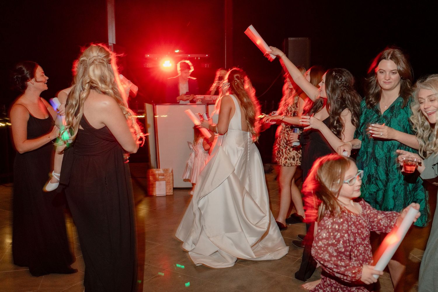 Wedding guests dancing and celebrating on the dance floor with a red light glowing in the background.