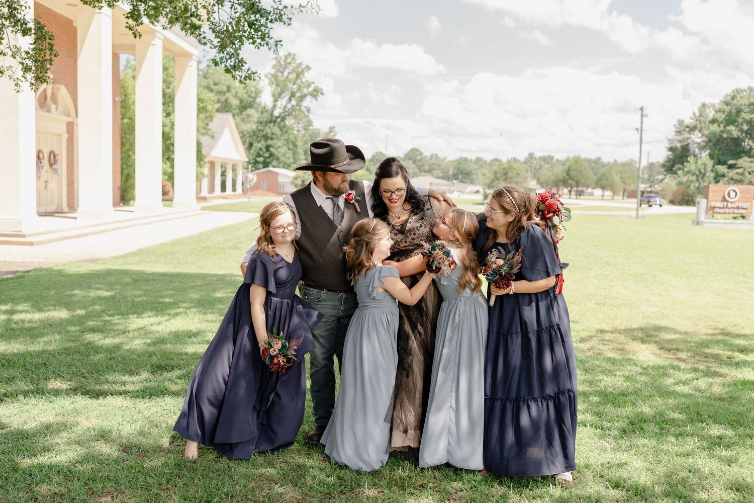 Wedding party members pose together on a sunny grassy lawn.