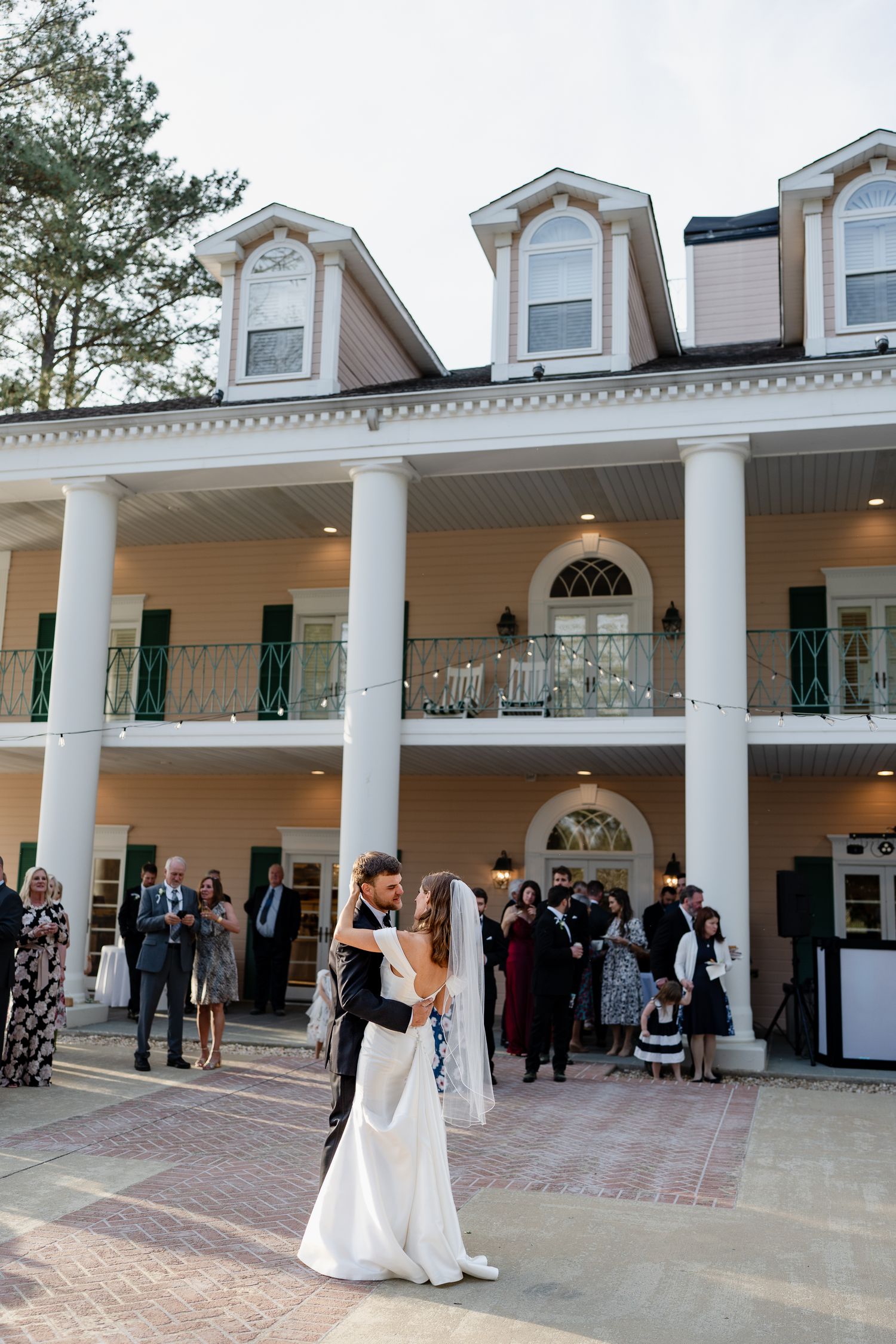 Wedding celebration outside grand Southern mansion with columns and balconies.