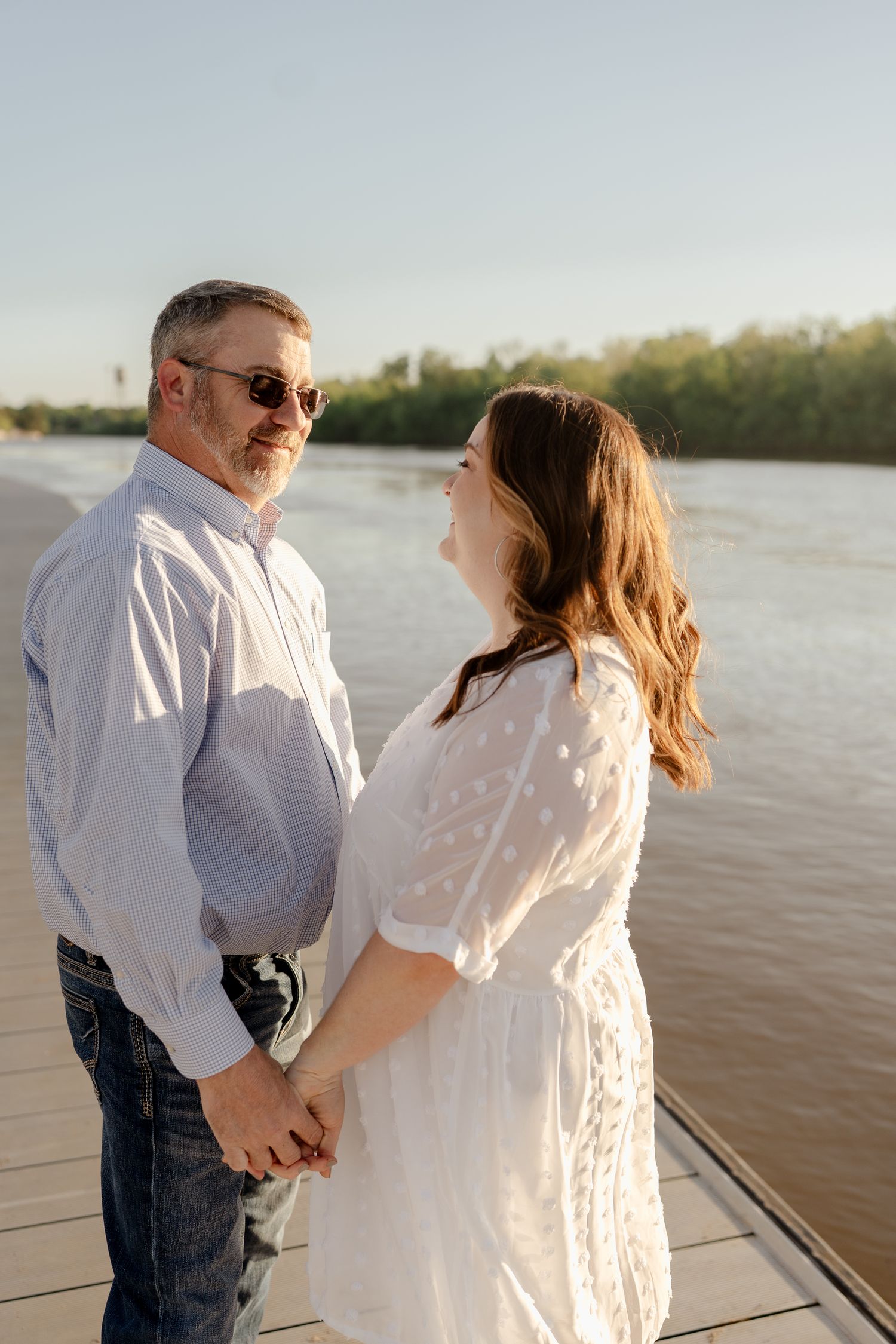 Two people share an intimate moment during a sunset photoshoot on a waterfront pier.