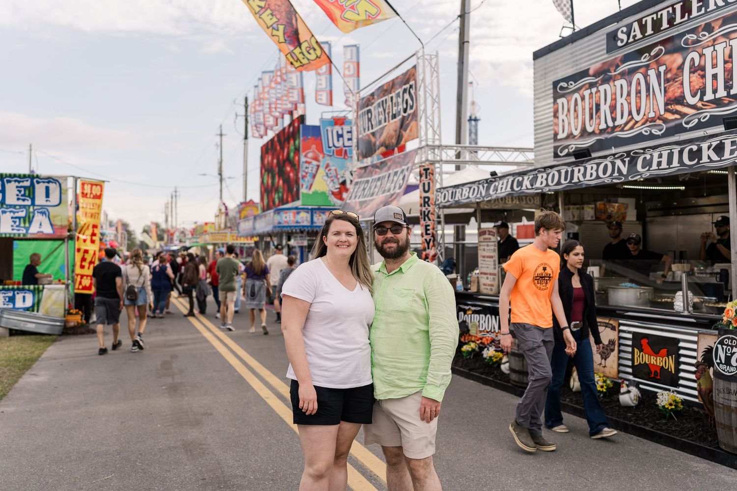 Busy food vendor area at a fair or carnival with colorful signs and food trucks selling bourbon chicken and other treats.