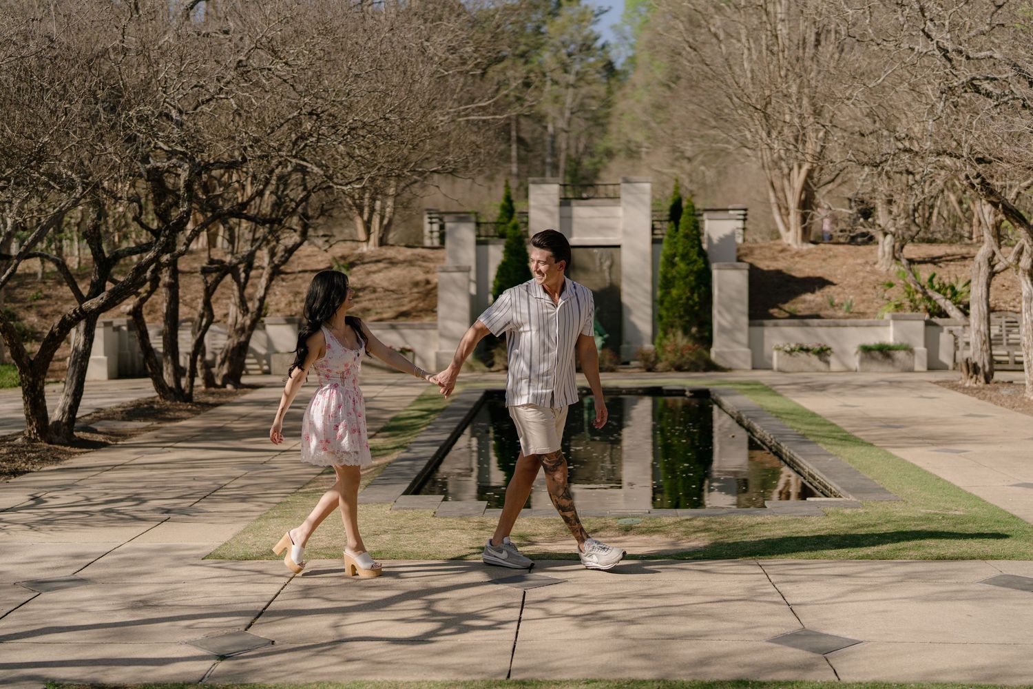 People walking and exercising on a tree-lined pathway in a park on a sunny day.