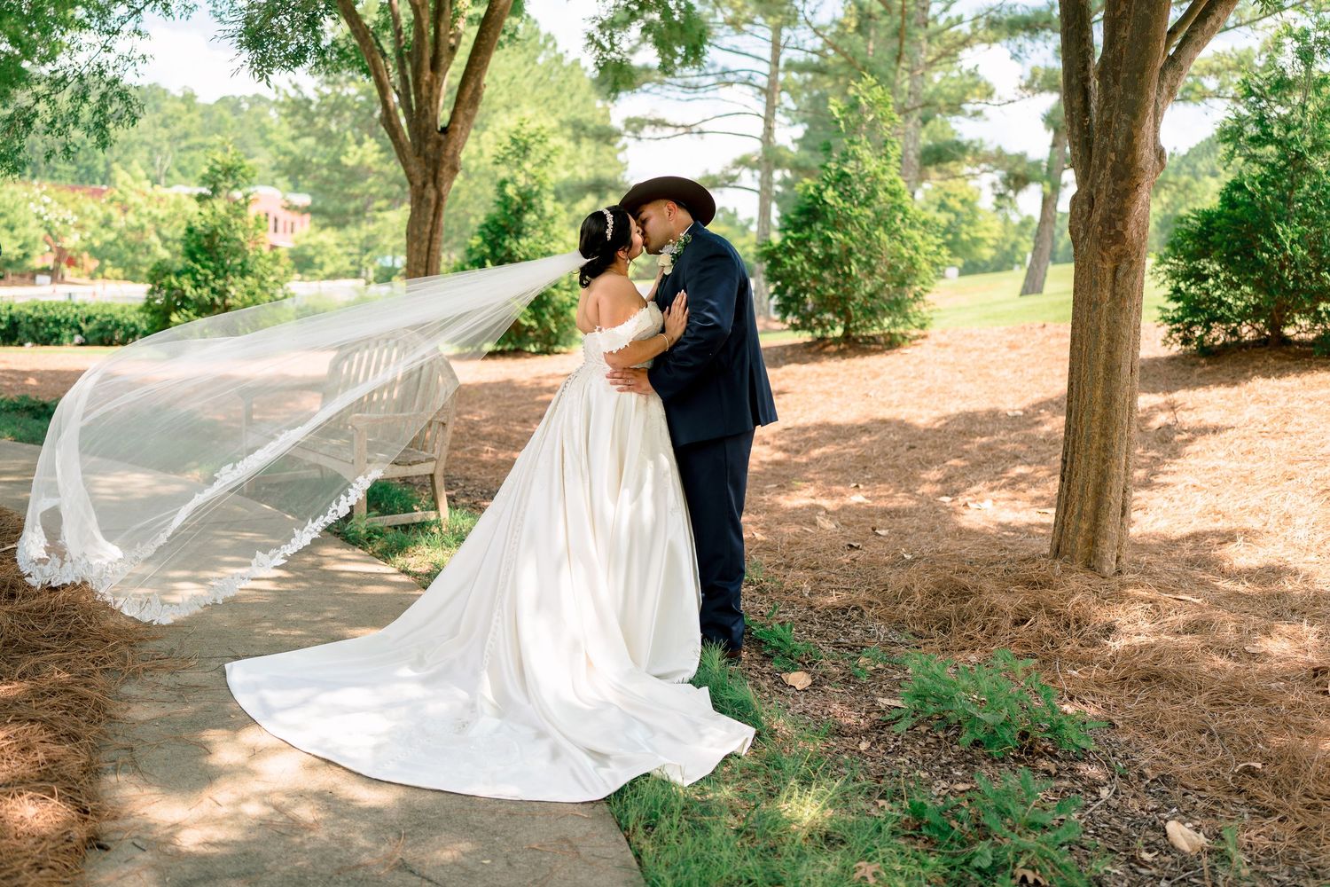 Romantic outdoor wedding photography session with billowing veil and tree-lined pathway.