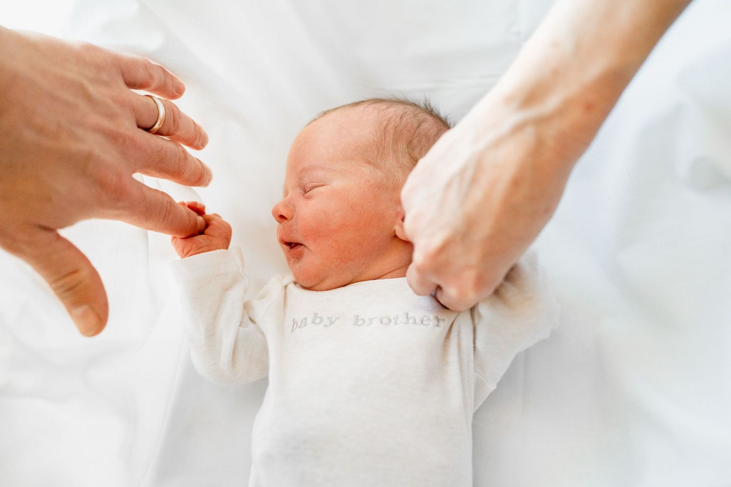 Gentle hands caressing a sleeping newborn dressed in white.