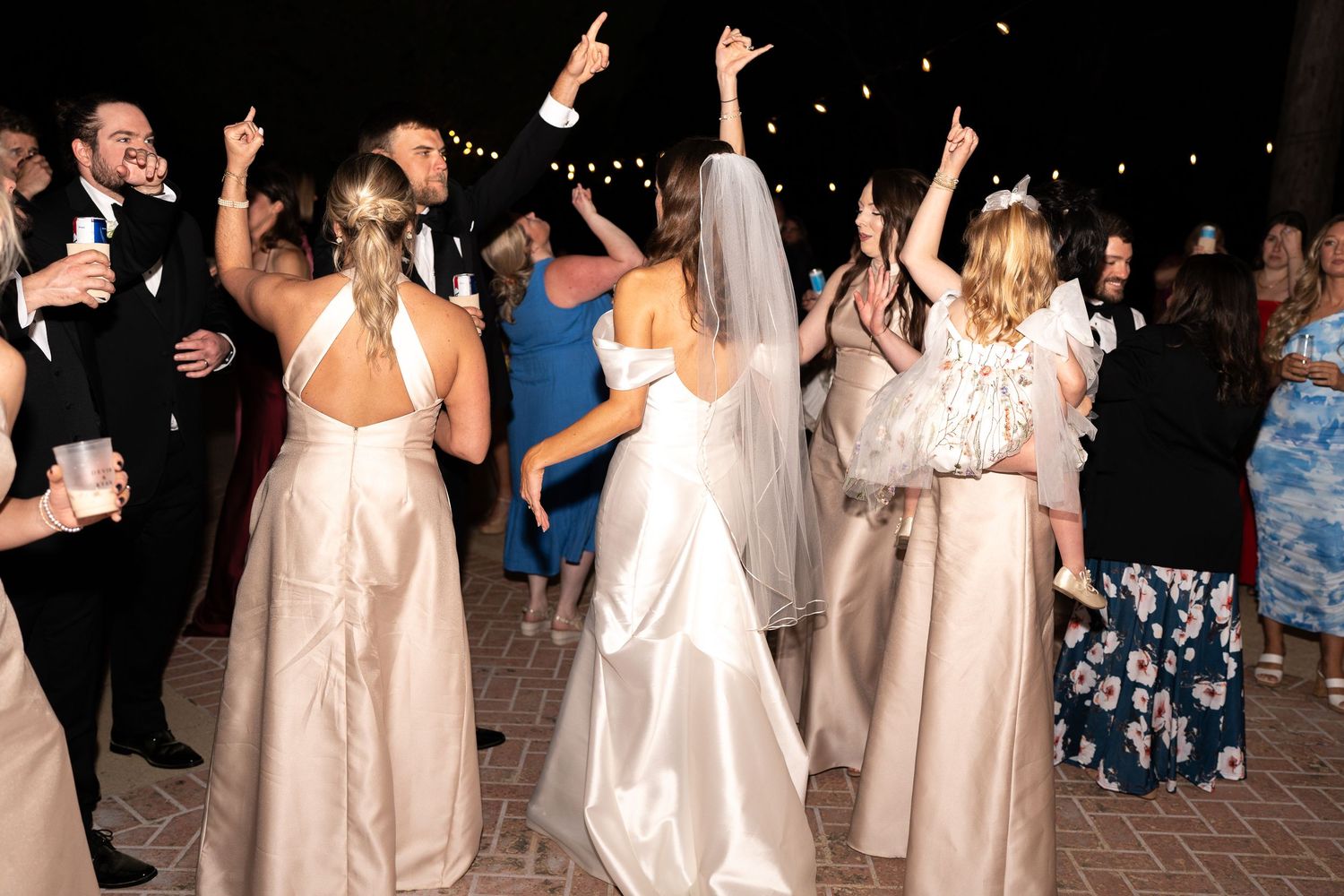 Group of bridesmaids in matching white dresses dancing at an evening reception.