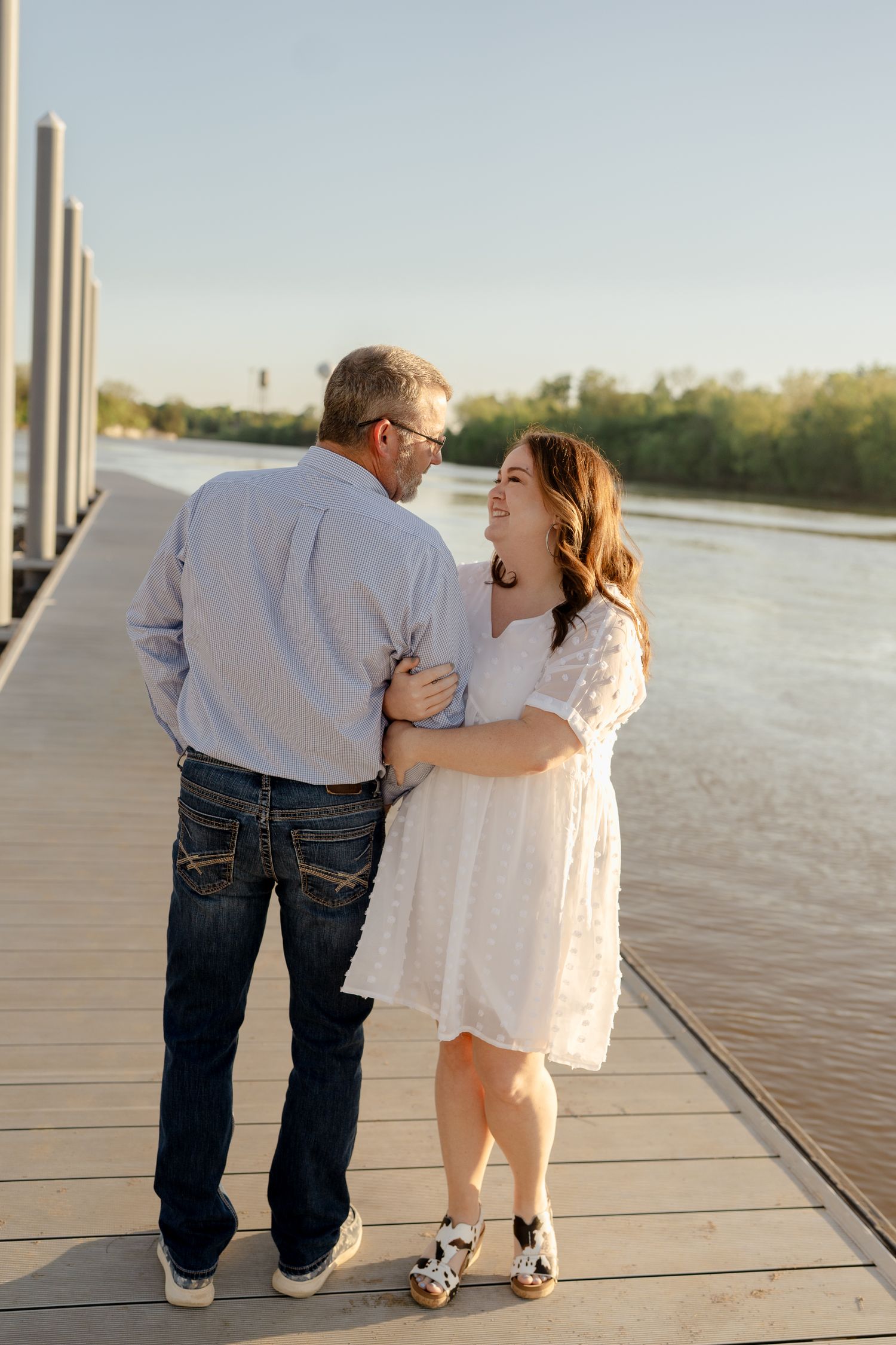 Two people walk together and share a close moment on a wooden pier by the water.