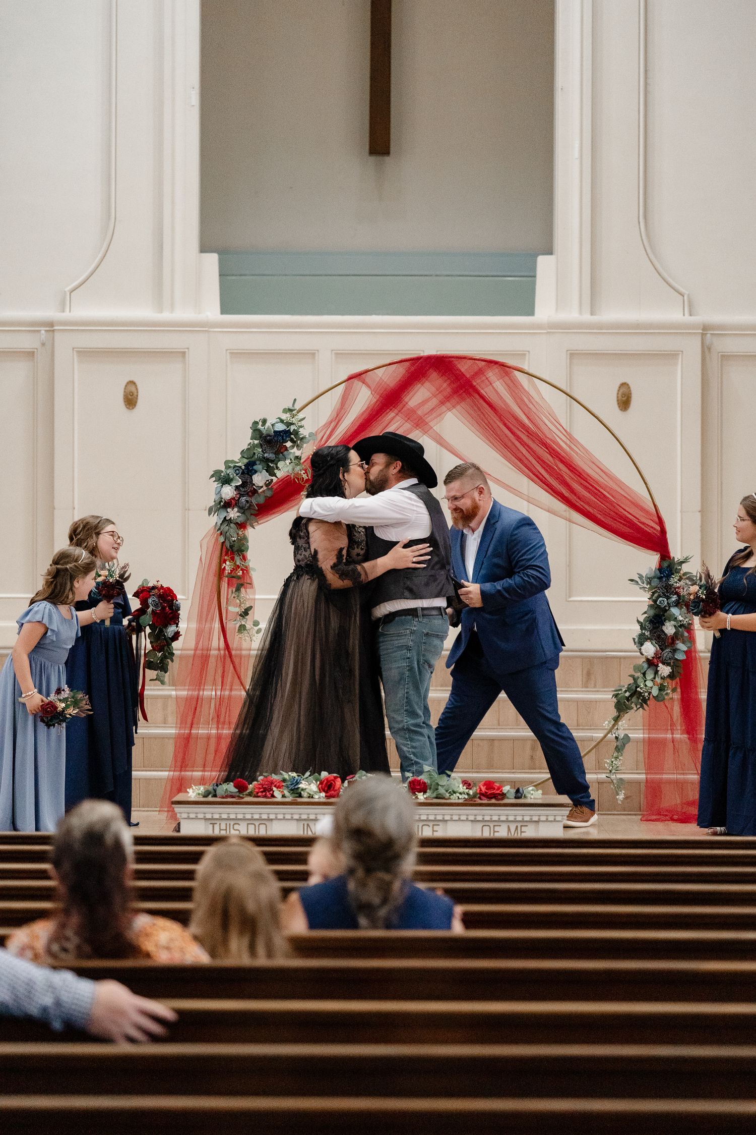 A series of romantic wedding ceremony kisses captured in a church with red drapery and wooden pews.