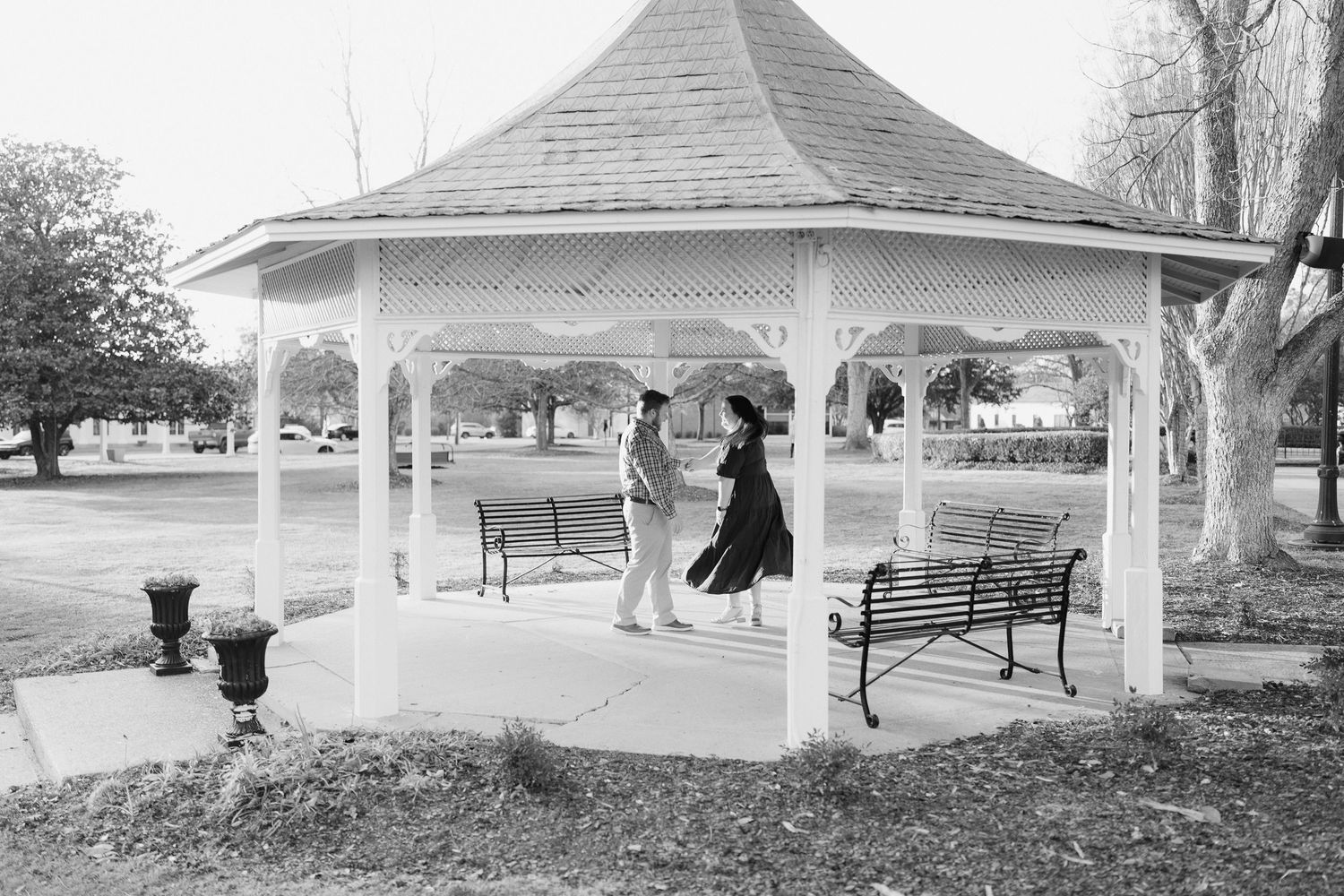Black and white photo of couple dancing under a white gazebo in a park.