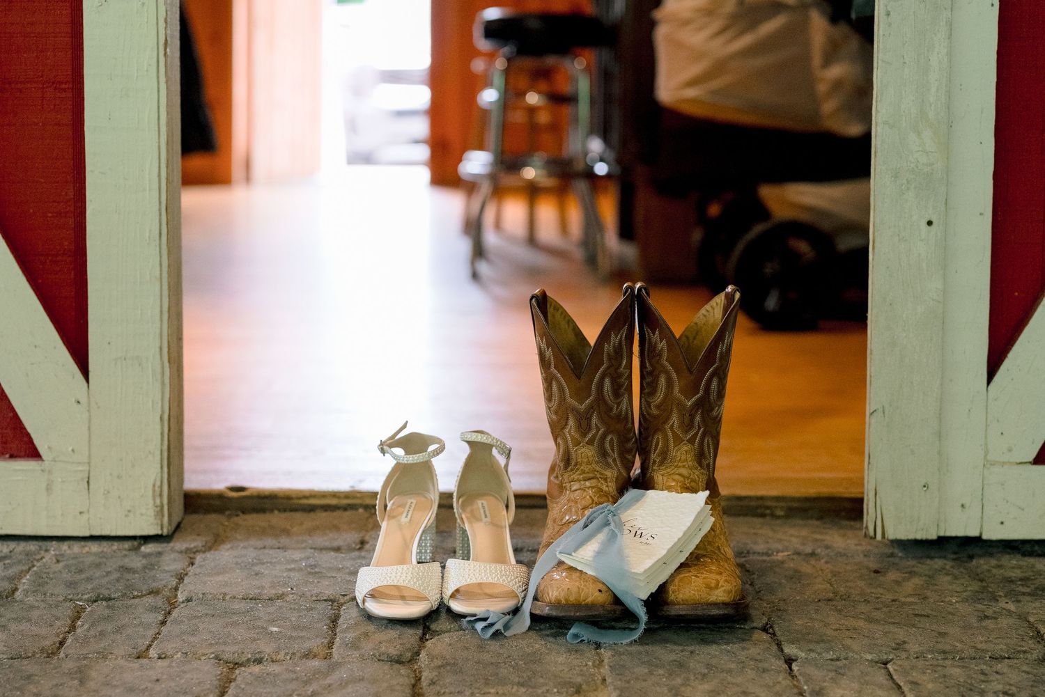 Bridal heels and cowboy boots with a blue garter at a rustic barn wedding venue doorway.