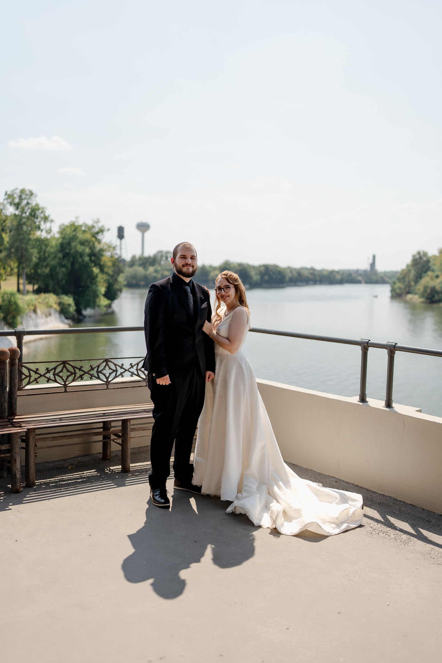 A wedding couple shares intimate moments on a waterfront balcony with scenic lake views in the background.