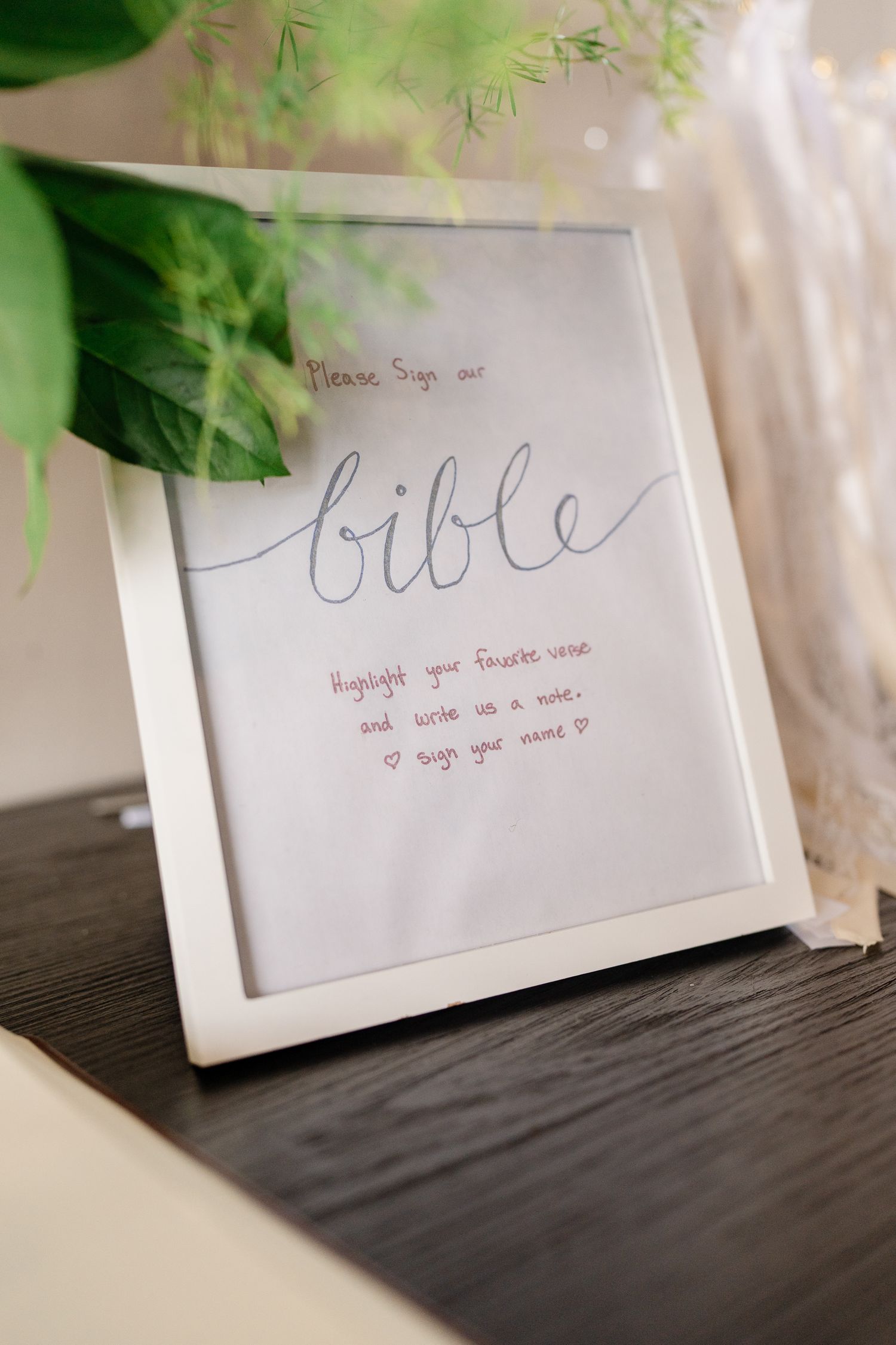 Handwritten wedding signs with elegant script text displayed against a dark surface with greenery accents.