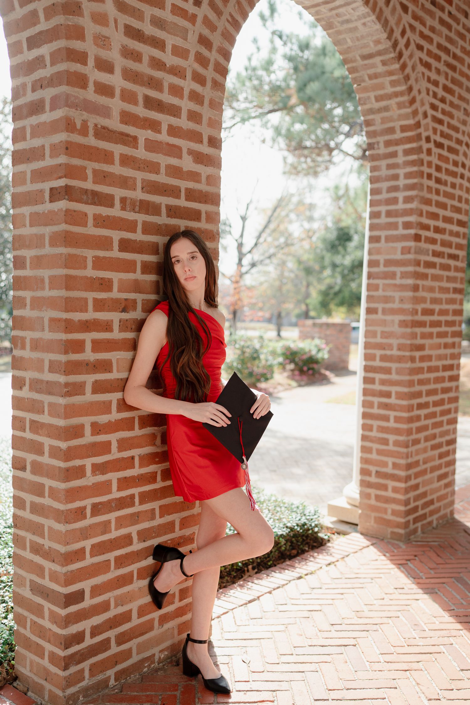 A figure in a red dress poses dramatically against brick columns in an outdoor walkway.