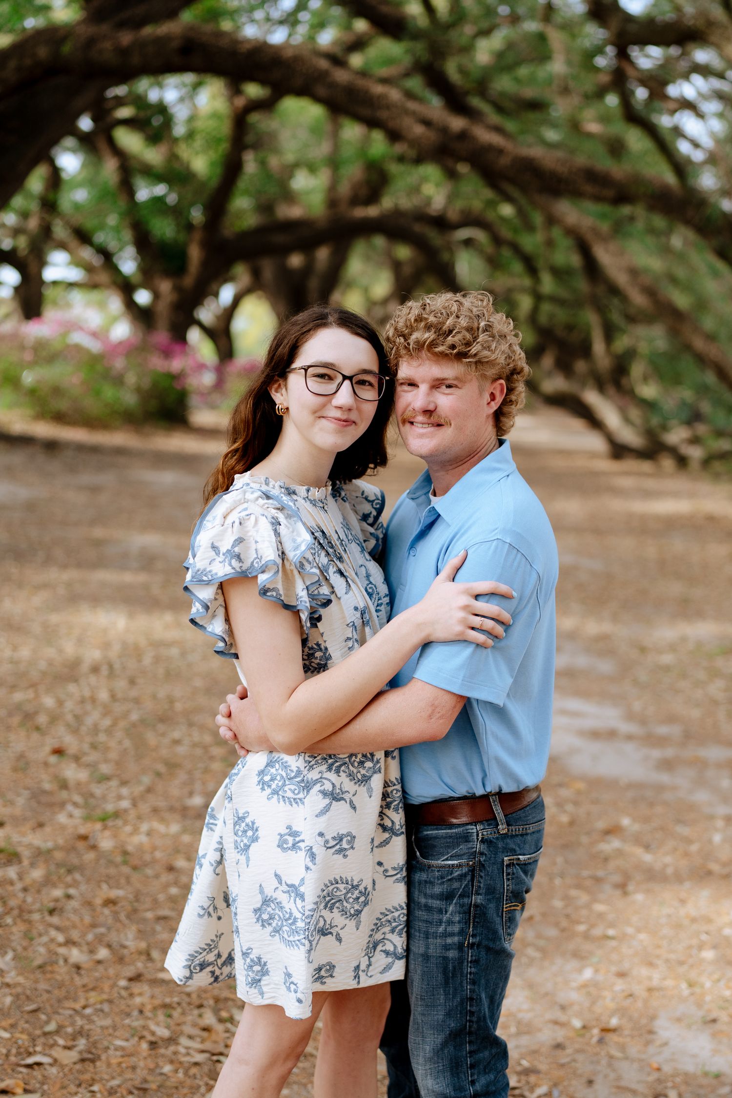 Sweet couple embraces while posing under sprawling oak trees.