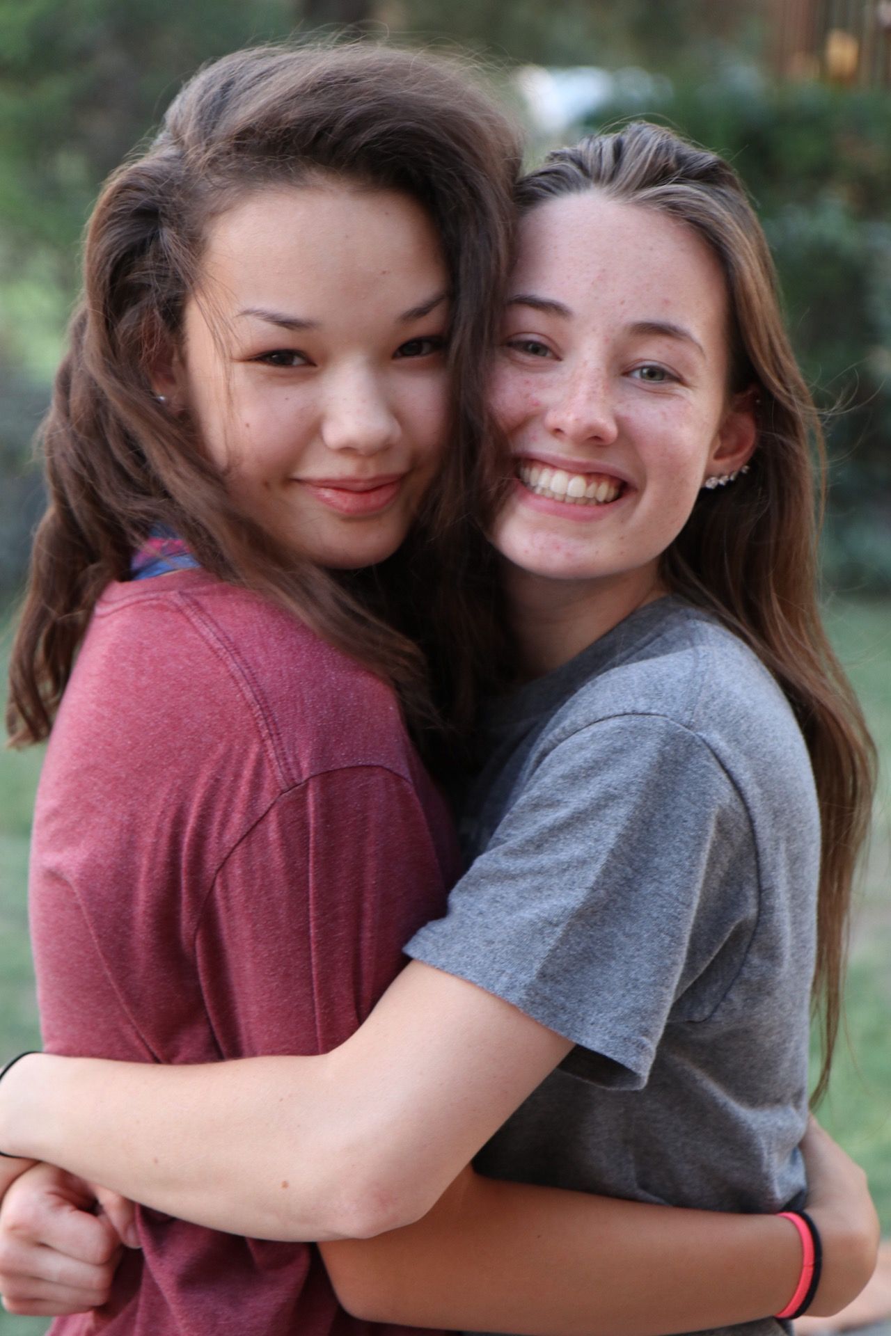 Two friends embrace and smile warmly for the camera outdoors.