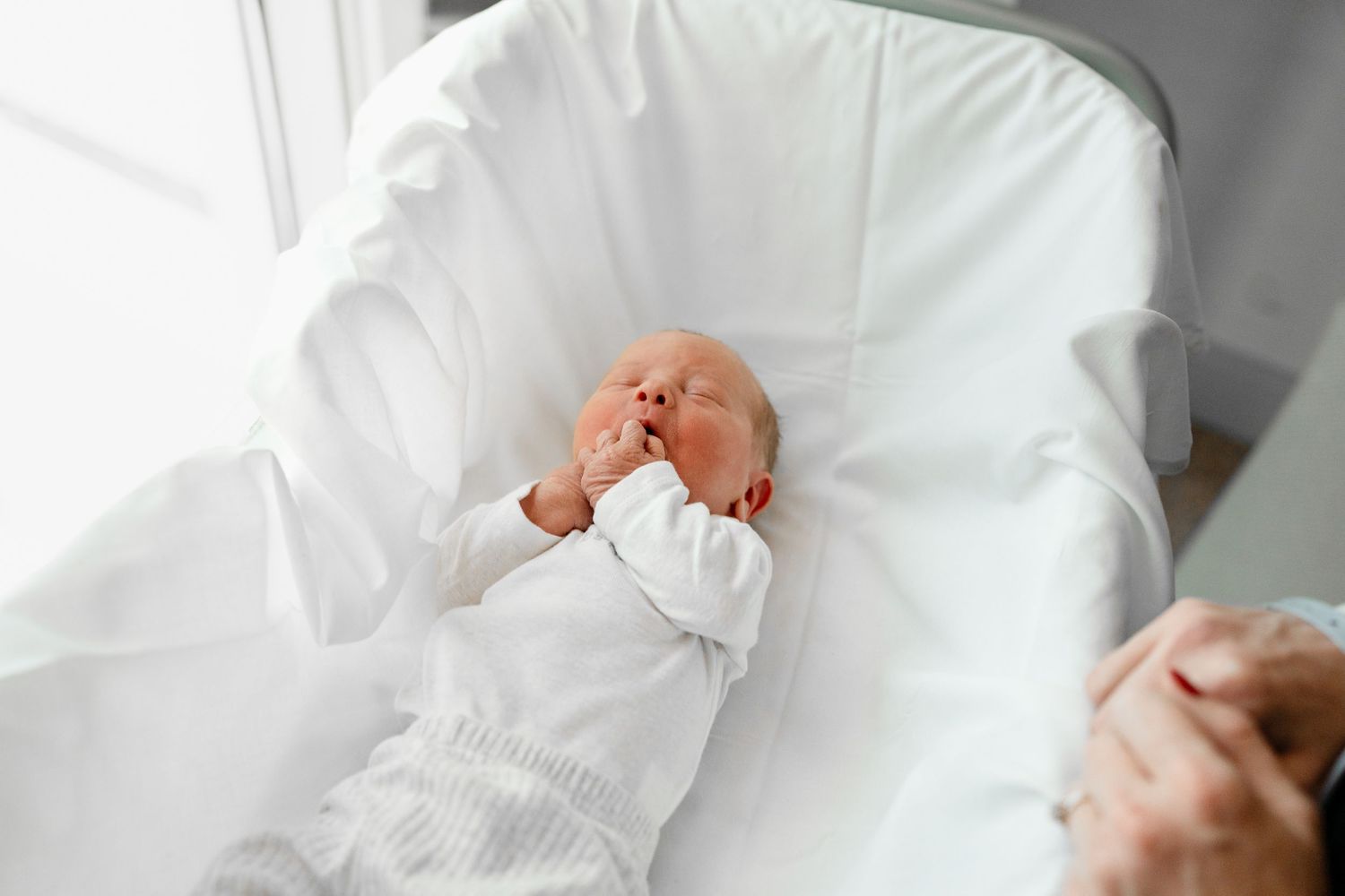 Hands tenderly adjusting newborn's white clothing and positioning on bed.