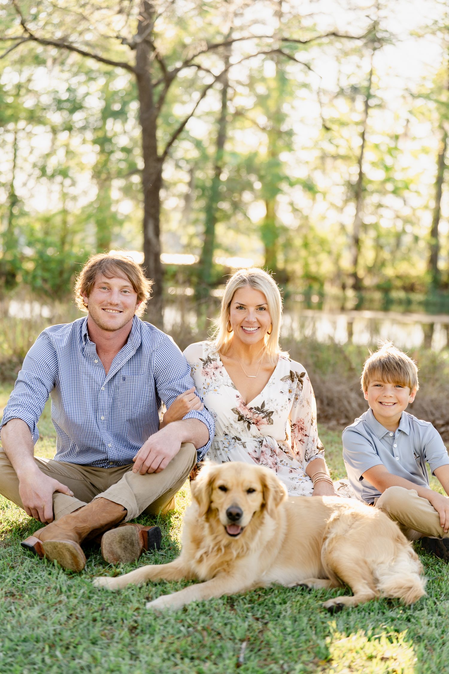 Family lounging on grass with their friendly golden retriever during a sunny outdoor photoshoot.