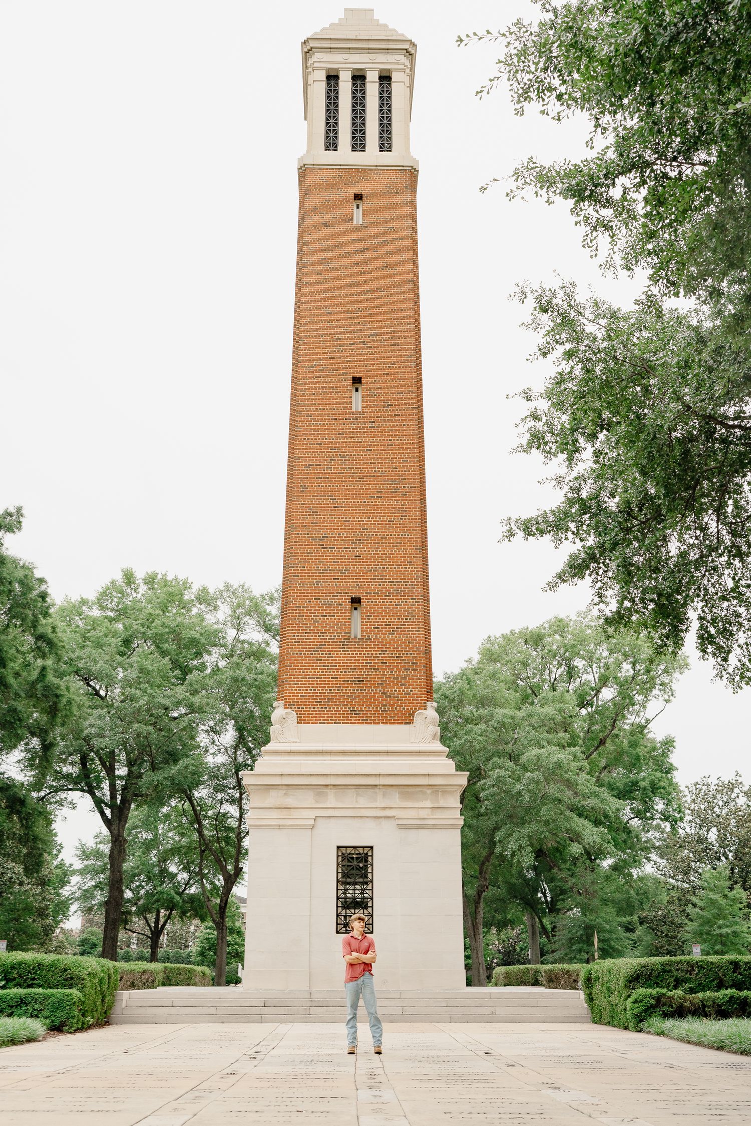 Tall brick bell tower with someone jumping playfully in front.