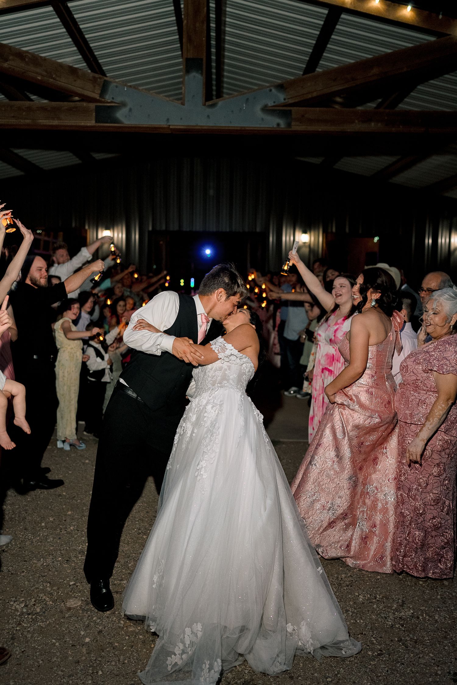 Bride and groom share a romantic kiss during sparkler send-off at rustic barn wedding reception at night.
