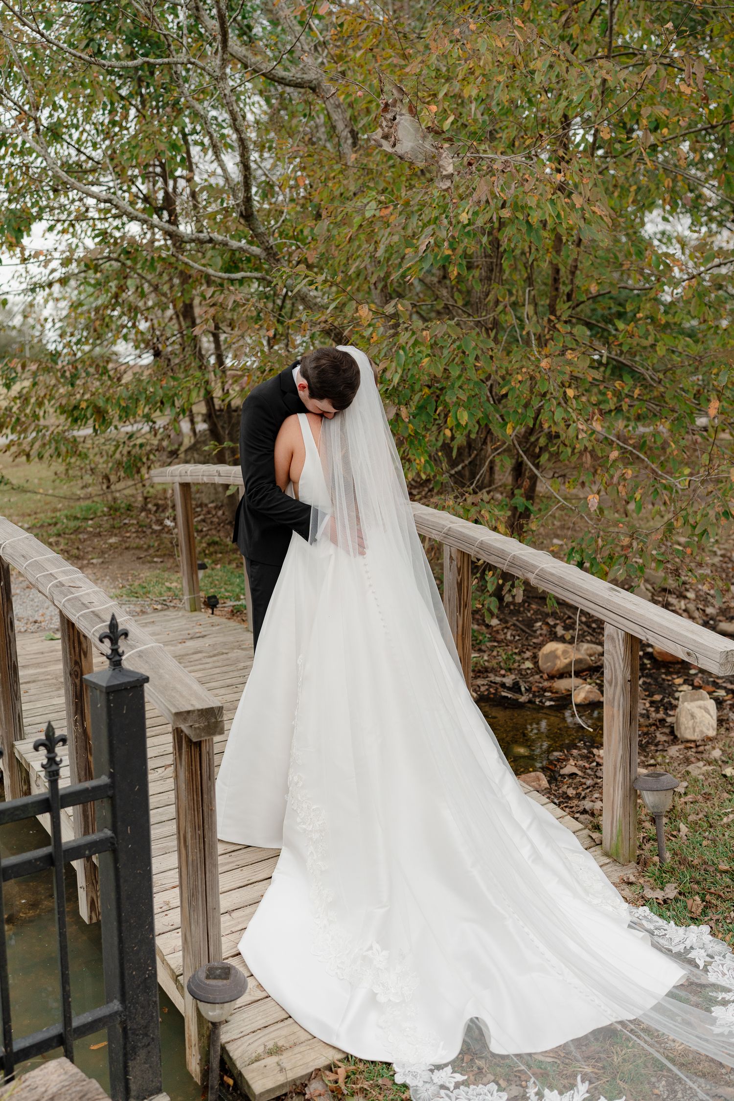 A flowing white wedding dress with a long veil cascades down wooden stairs surrounded by autumn foliage.