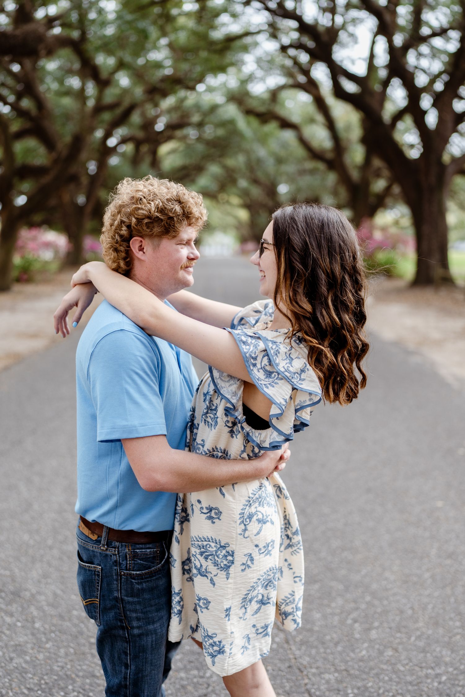 Dancing couple in light blue and floral print outfits share sweet moments under oak trees.