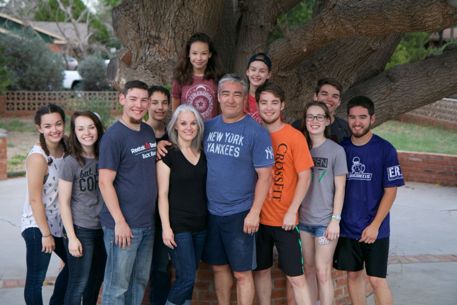A group photo with people standing together in front of a tree, wearing casual clothes and t-shirts.
