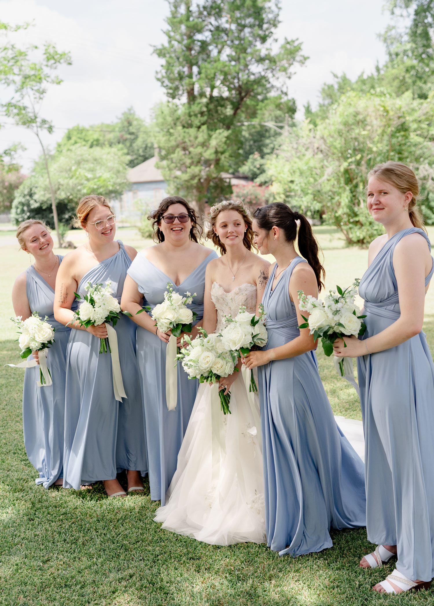 Wedding party in light blue bridesmaid dresses and white wedding gown gather outdoors for candid group photos.