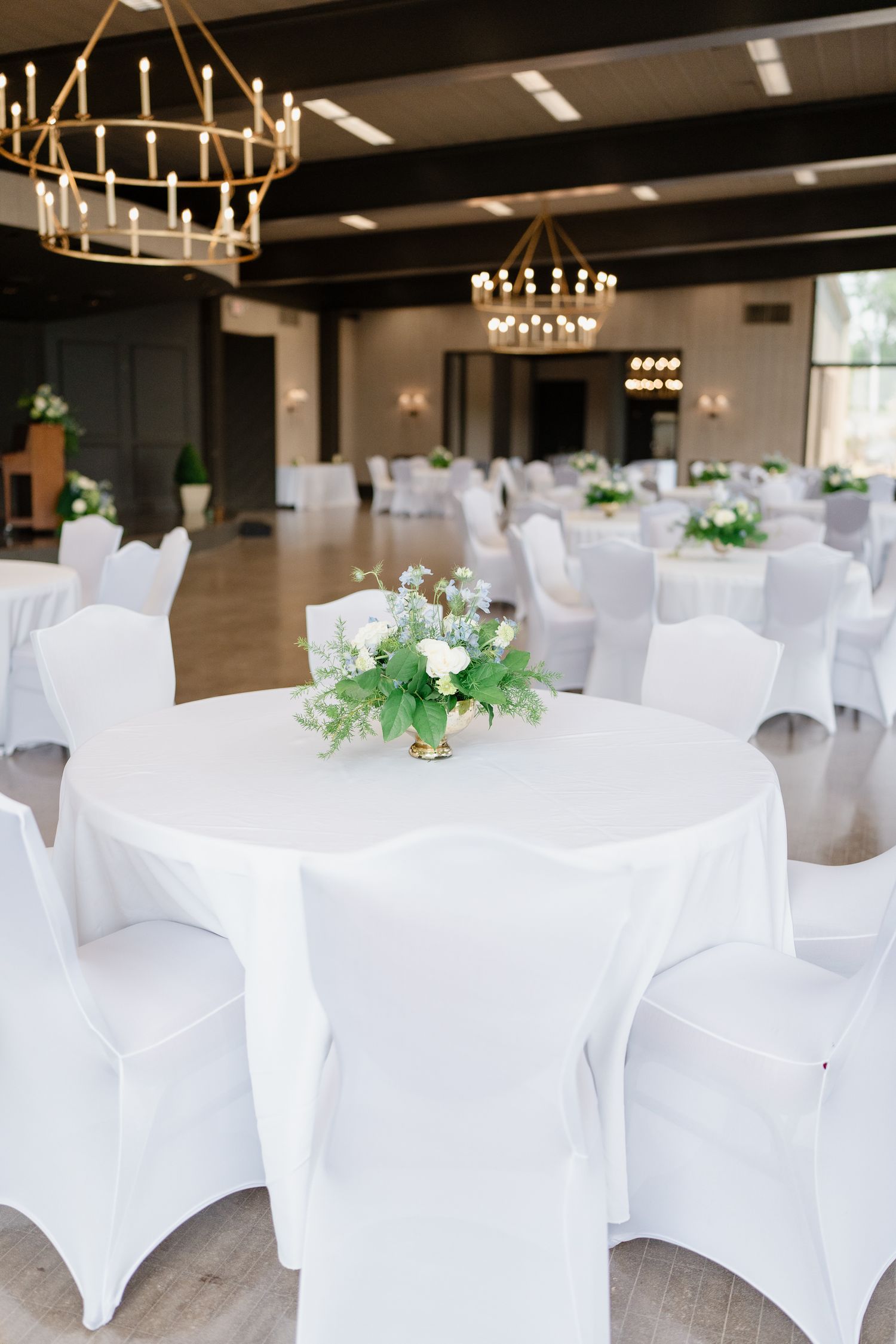 White spandex chair covers and elegant chandeliers decorate an elegant event space set up for a formal reception.