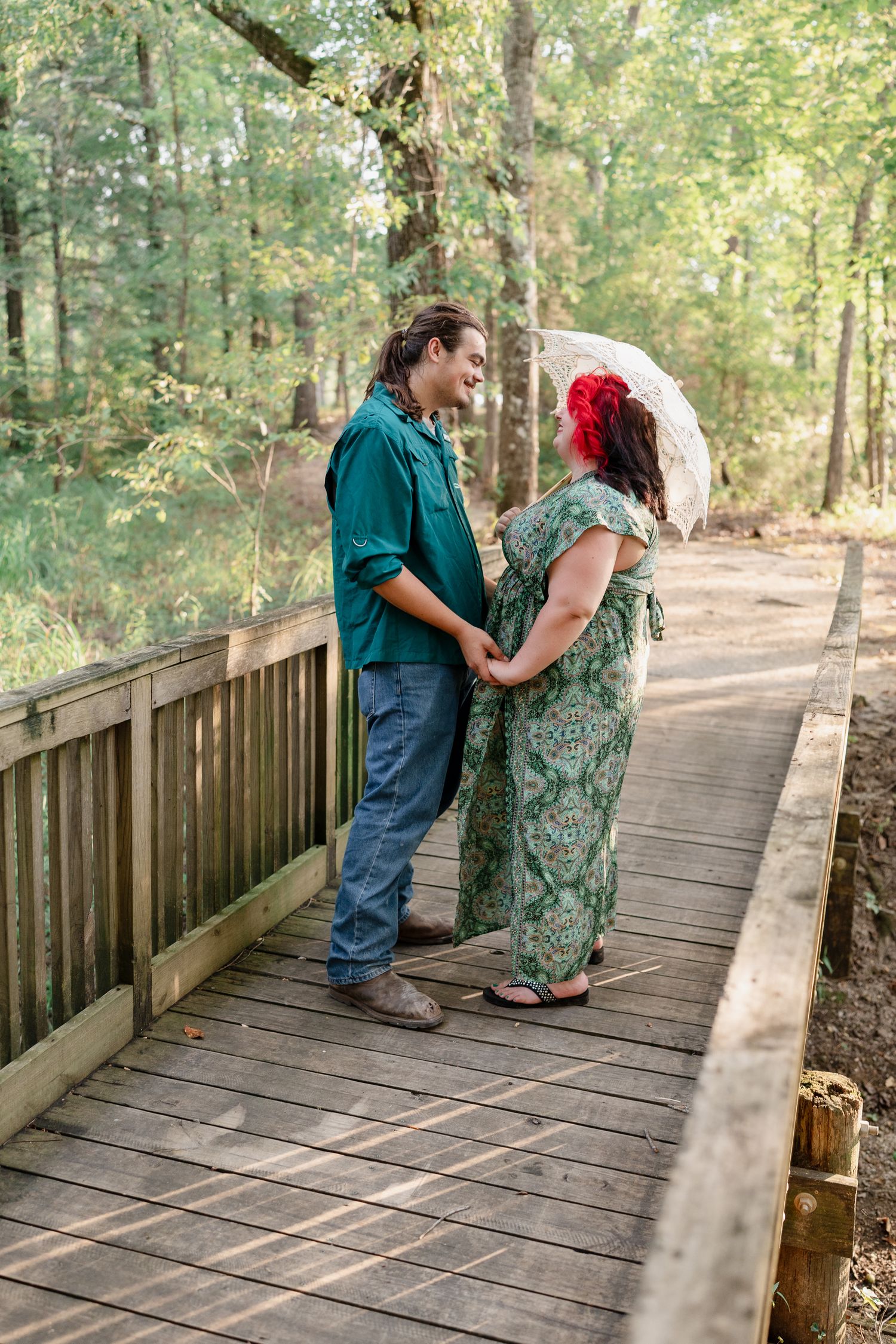 A couple shares tender moments on a rustic wooden bridge surrounded by green forest scenery.