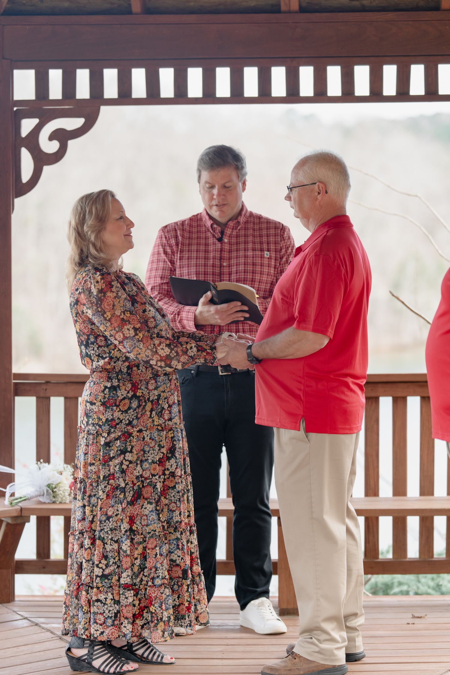 Couple exchanging vows in a wooden gazebo with an officiant during an intimate outdoor wedding ceremony.