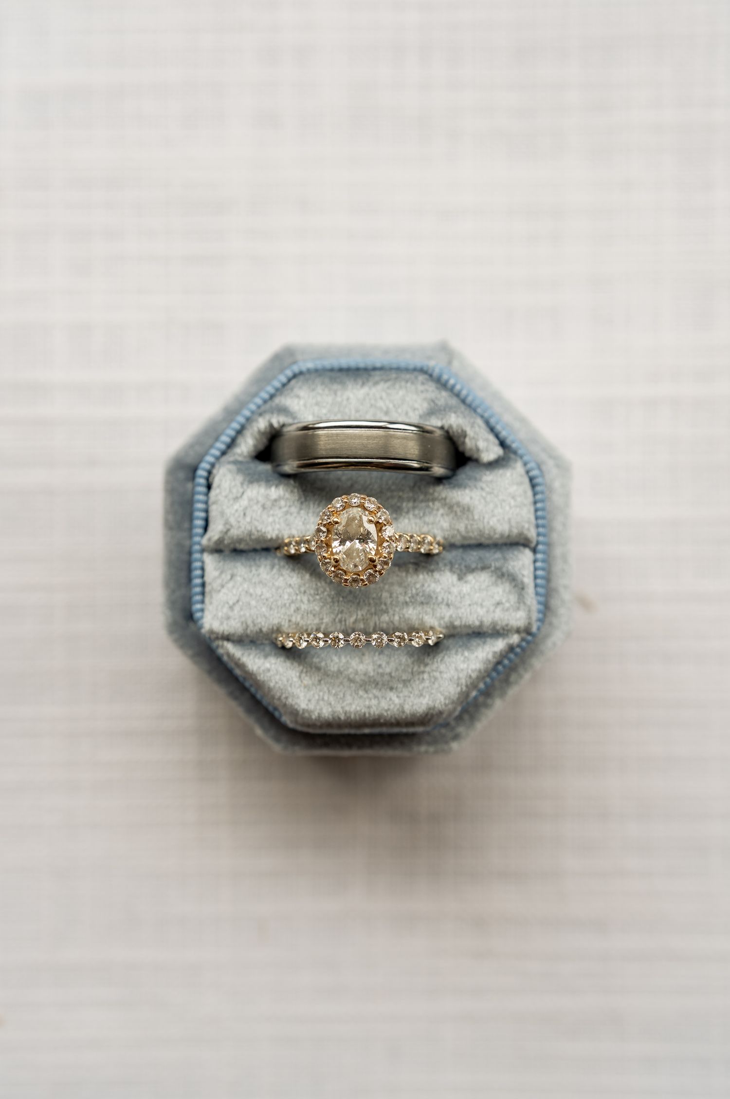 Blue velvet octagonal ring box holding a diamond halo engagement ring, wedding band, and delicate diamond eternity ring.
