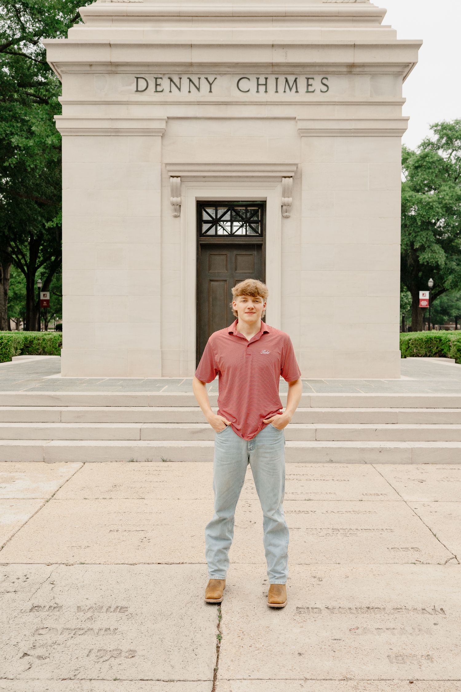 Someone poses in front of the historic Denny Chimes building wearing a coral polo shirt.