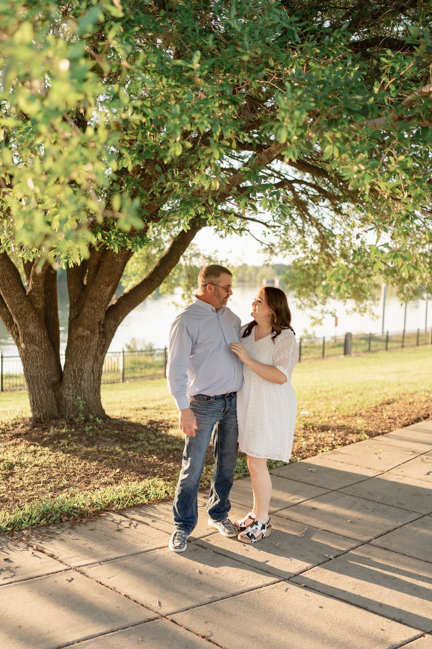 A couple sharing a romantic moment on a path under a leafy tree.