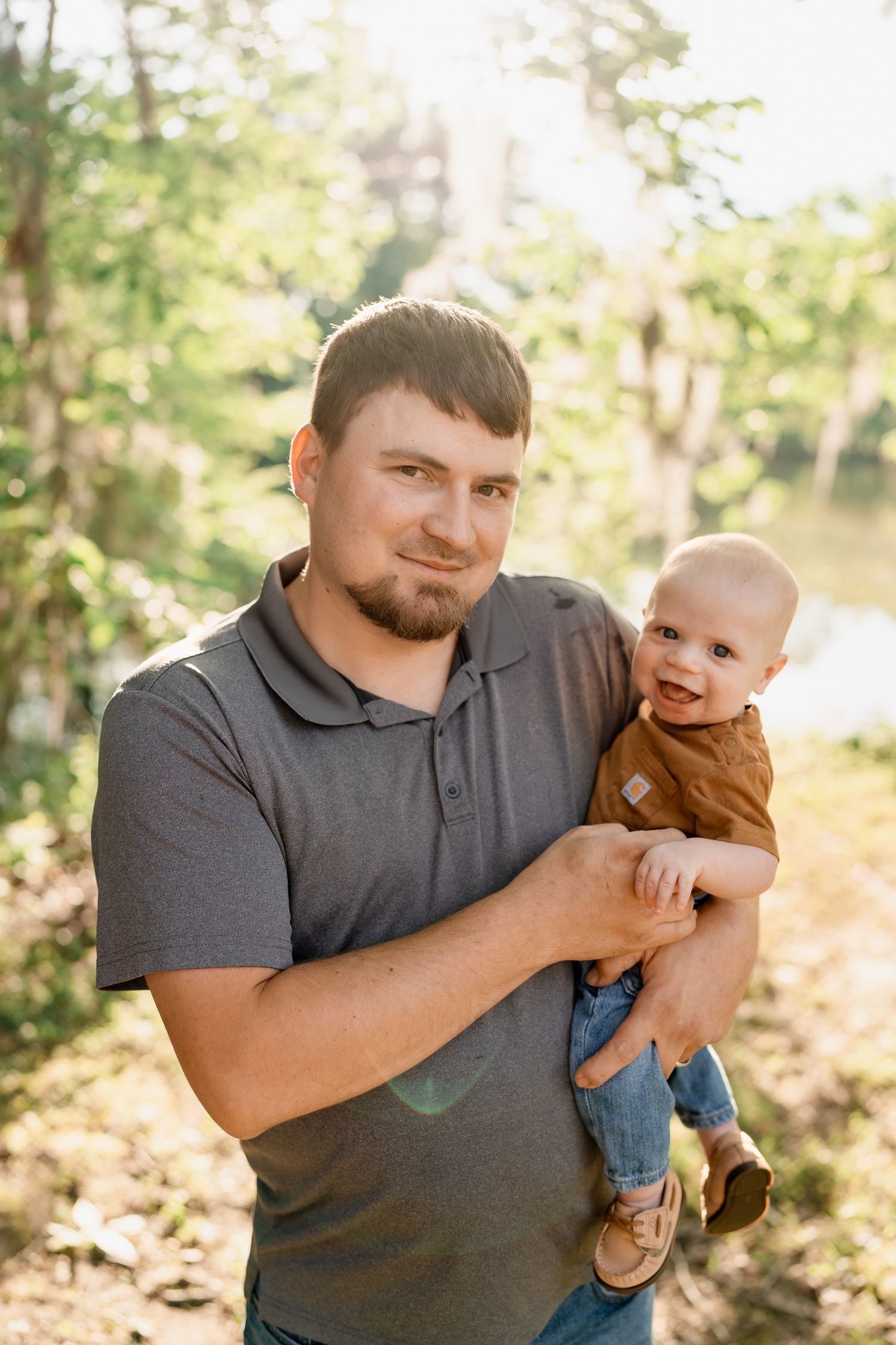 Father holds baby during outdoor photo session in wooded setting.