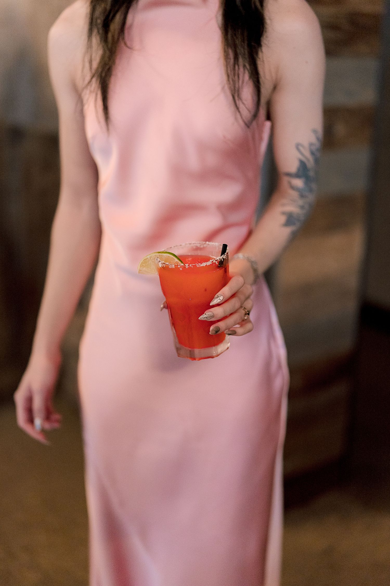 Bridesmaid in pink satin dress holds red cocktail garnished with citrus slice.