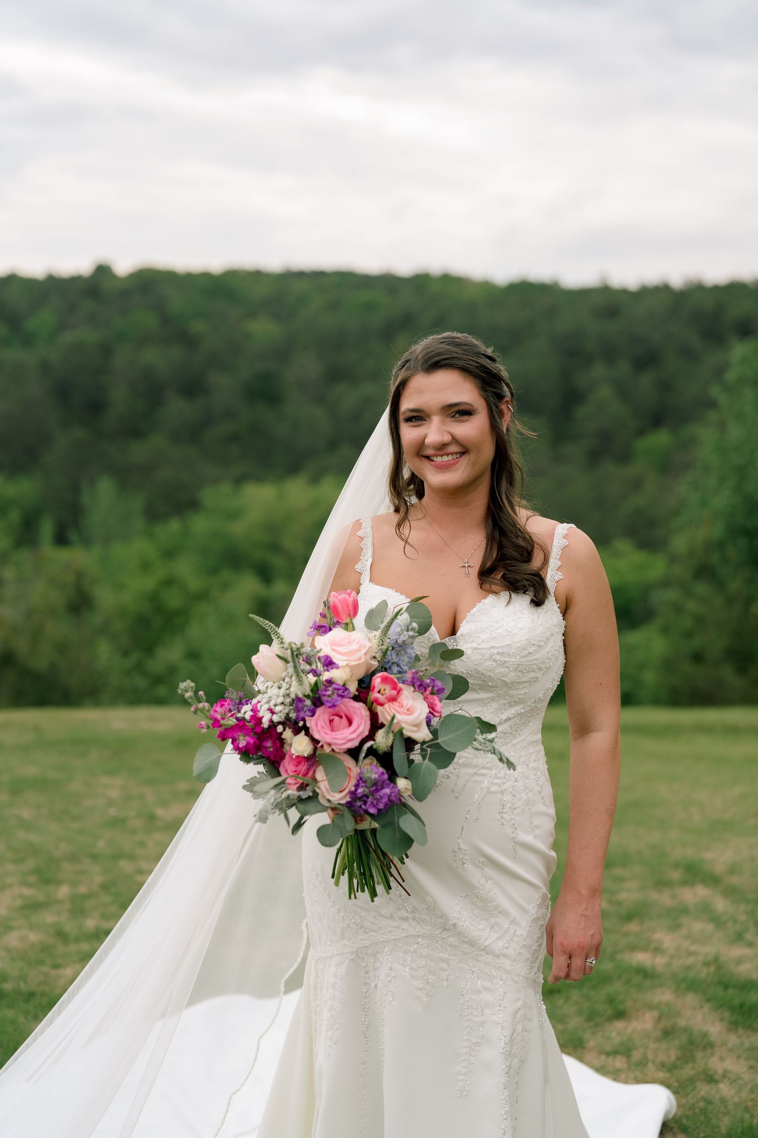 Radiant bride in white lace gown holds vibrant pink and purple bouquet with veil flowing.