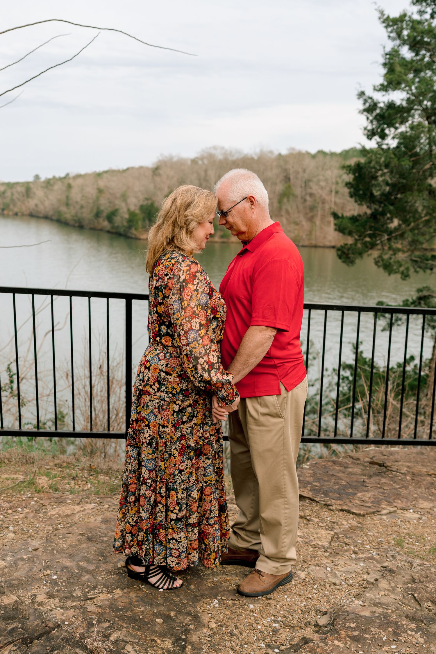 Older couple holding hands and praying together at a scenic riverside overlook.